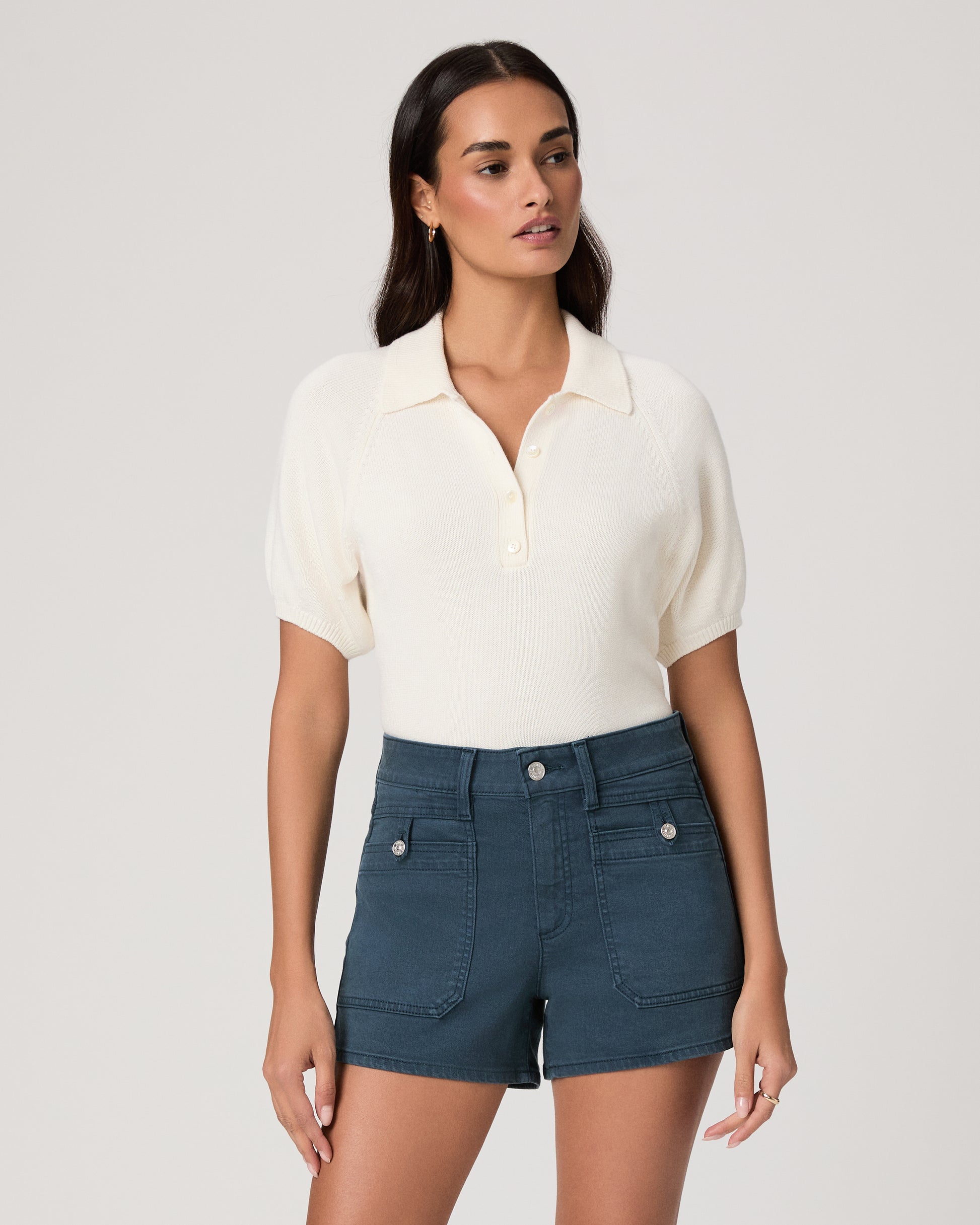 Woman wearing a white polo shirt and blue shorts on a plain background