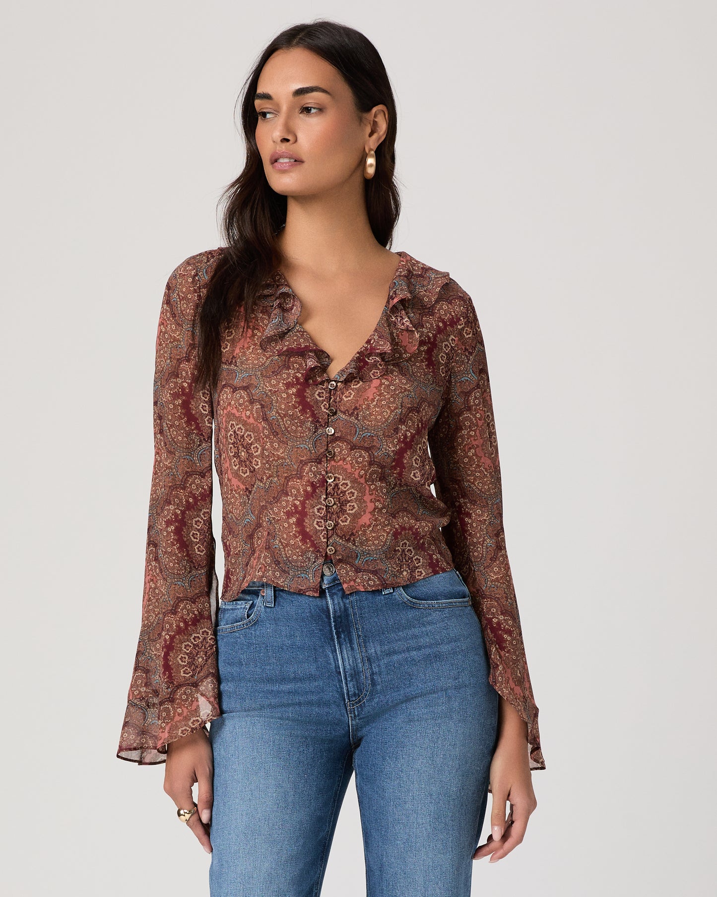 Woman wearing a patterned blouse and blue jeans on a plain background