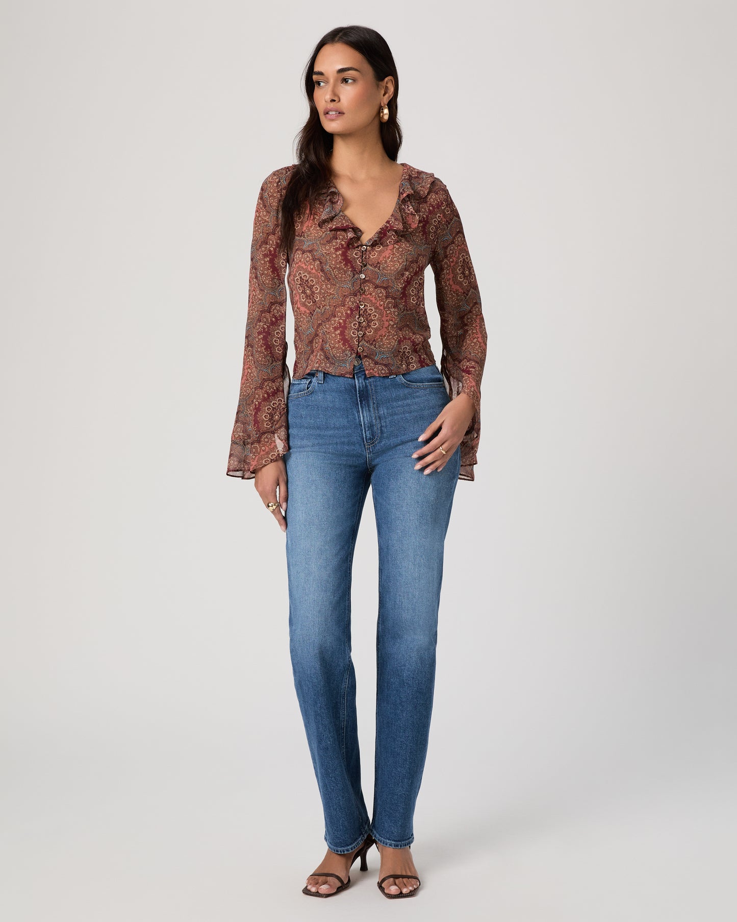 Woman wearing a patterned blouse and blue jeans on a plain background