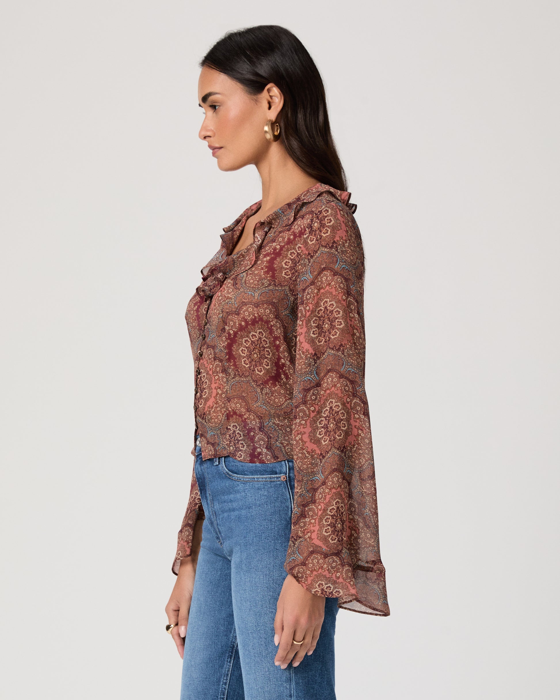 Woman wearing a patterned blouse and blue jeans on a plain background