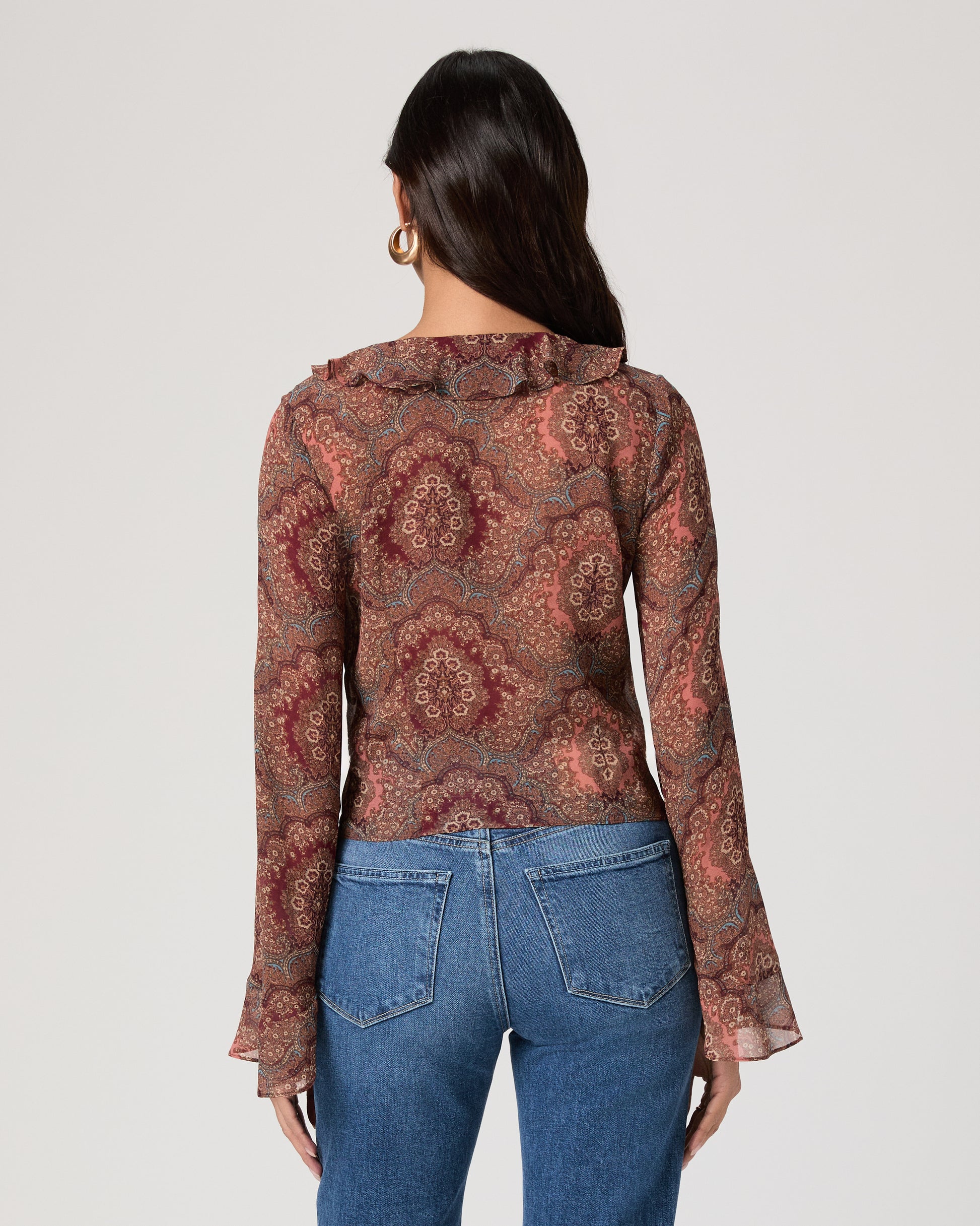 Woman wearing a patterned blouse and blue jeans on a plain background