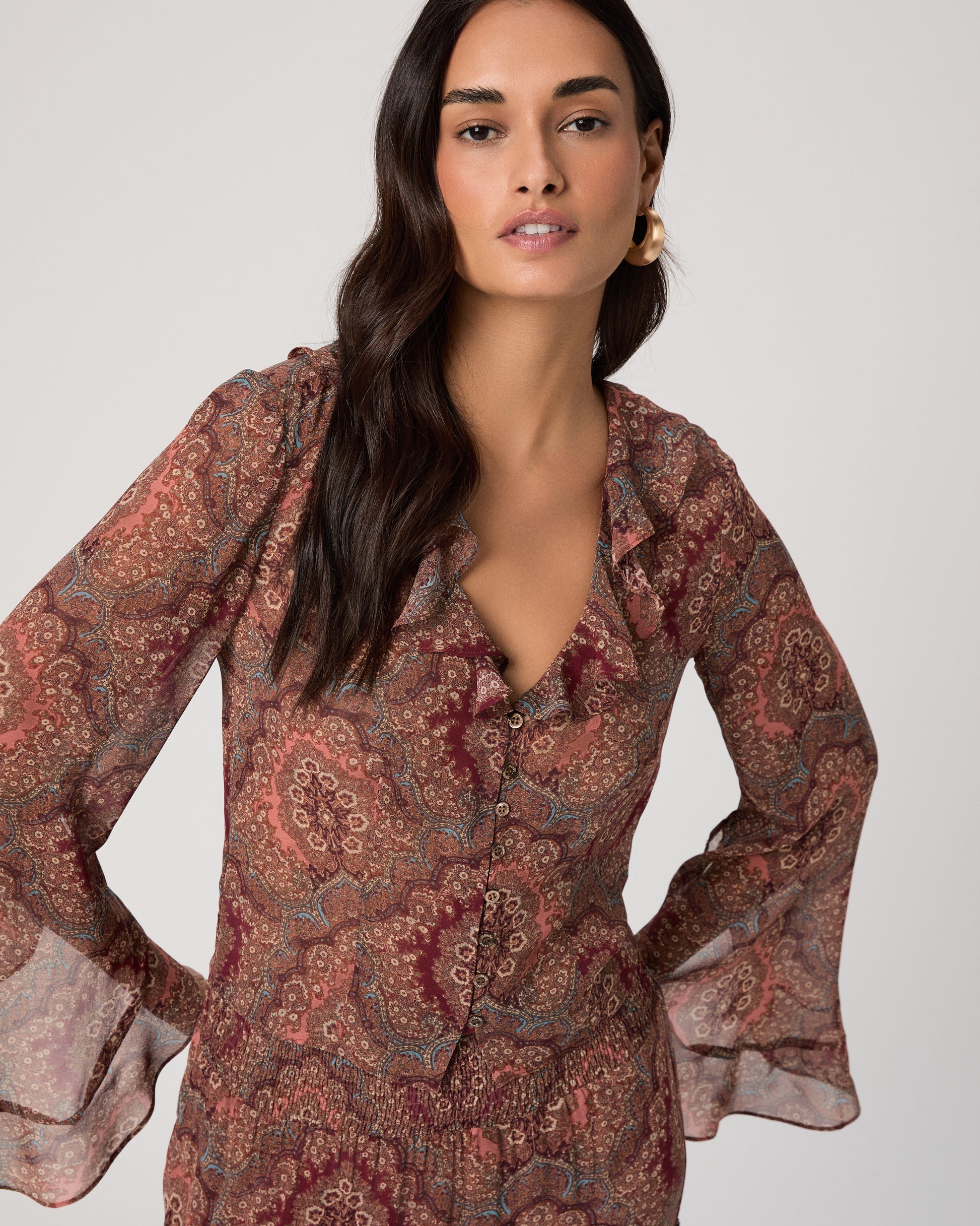 Woman wearing a patterned blouse and blue jeans on a plain background