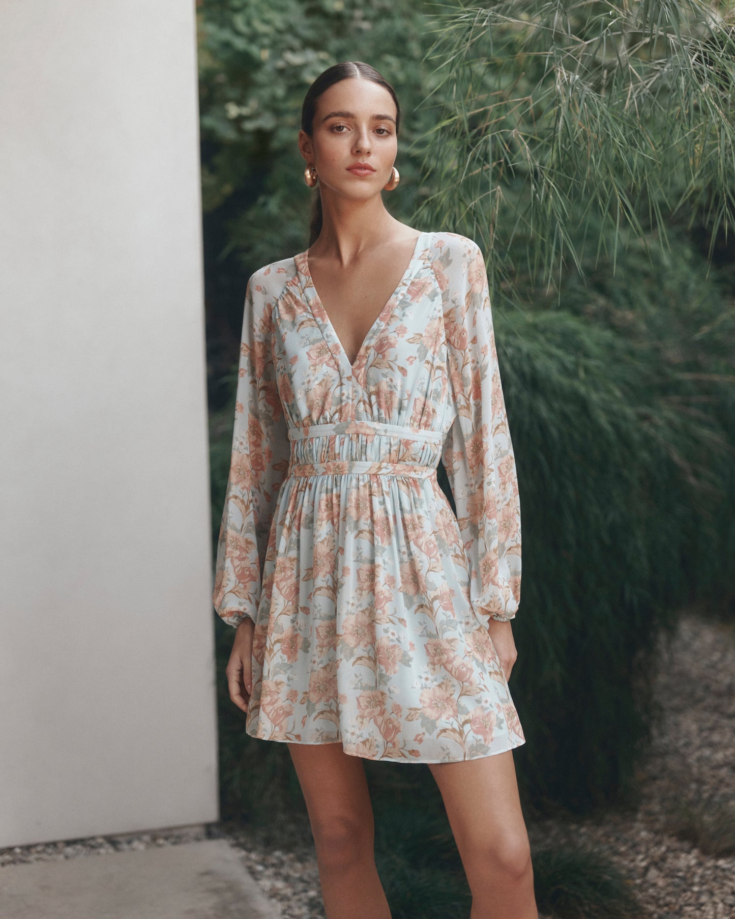 Woman wearing a floral dress standing outdoors with greenery in the background
