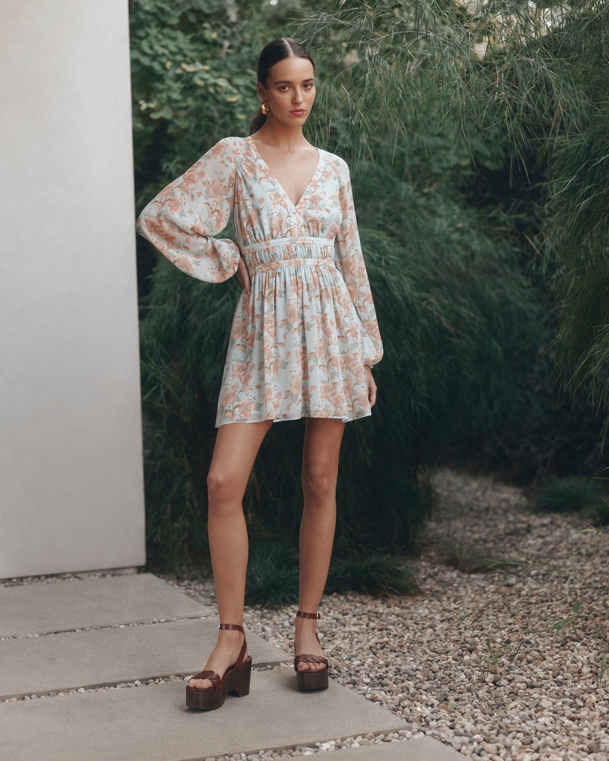 Woman in a floral dress standing outdoors with greenery in the background