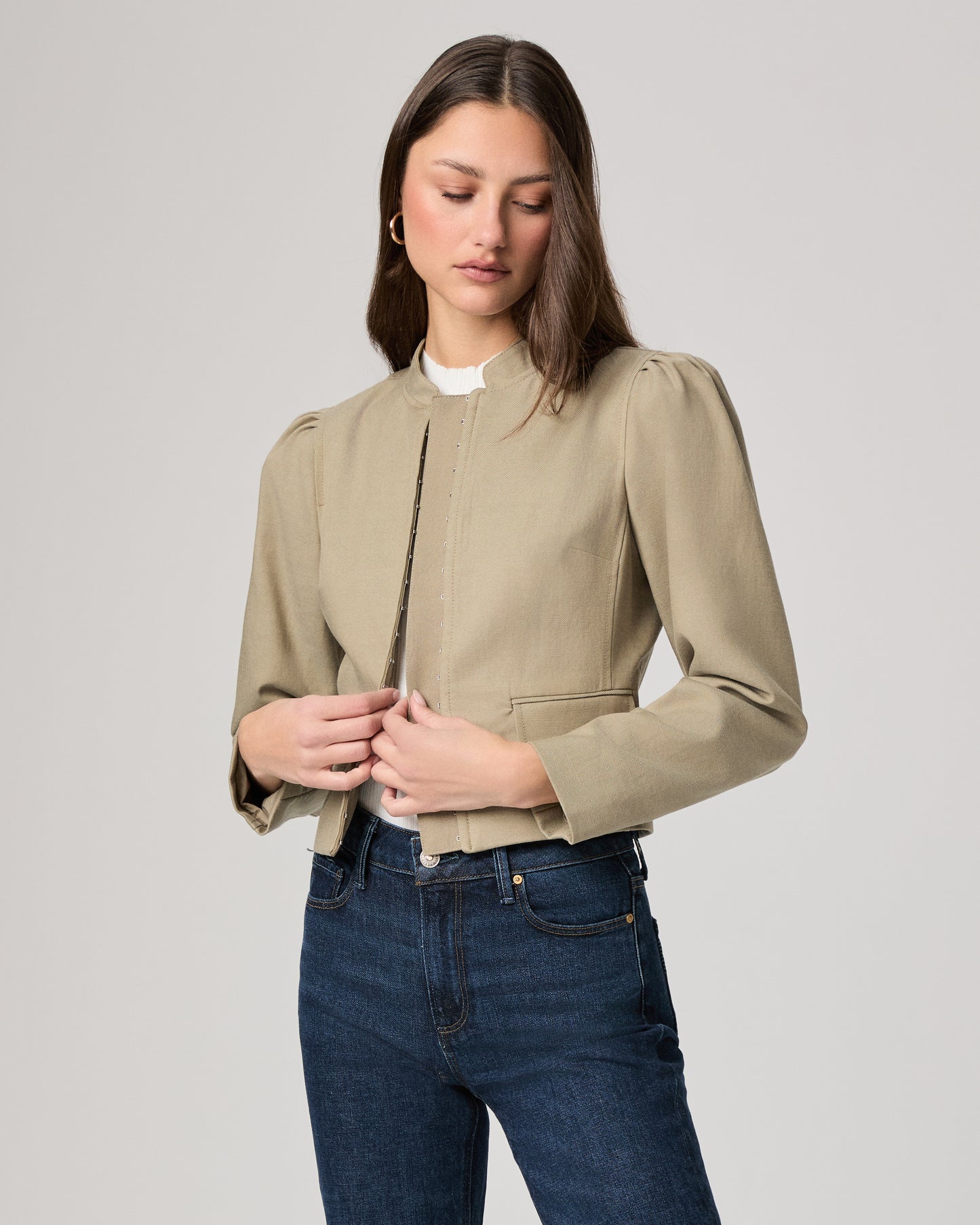 Woman wearing a light green jacket and dark blue jeans on a white background