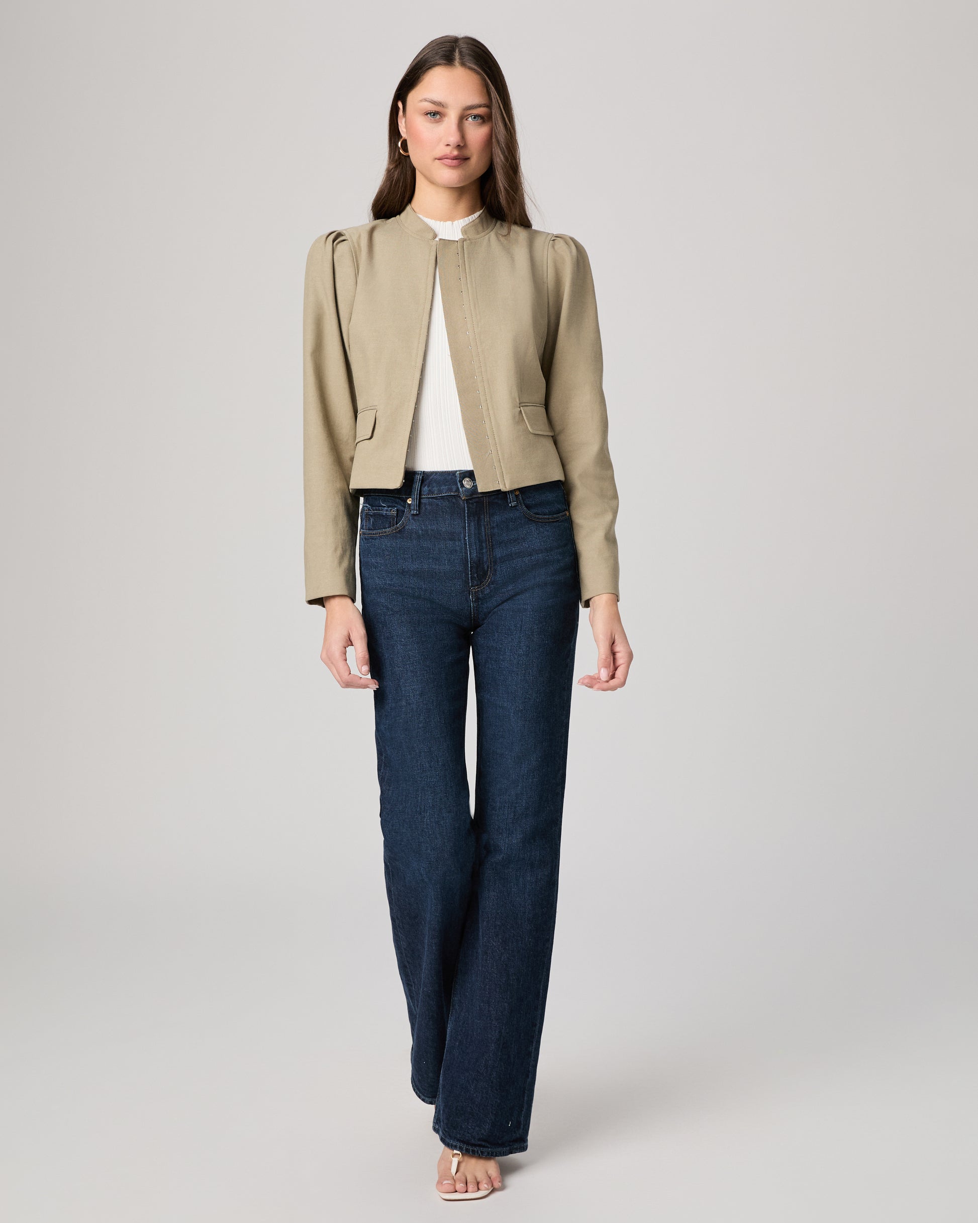 Woman wearing a light green jacket and dark blue jeans on a white background