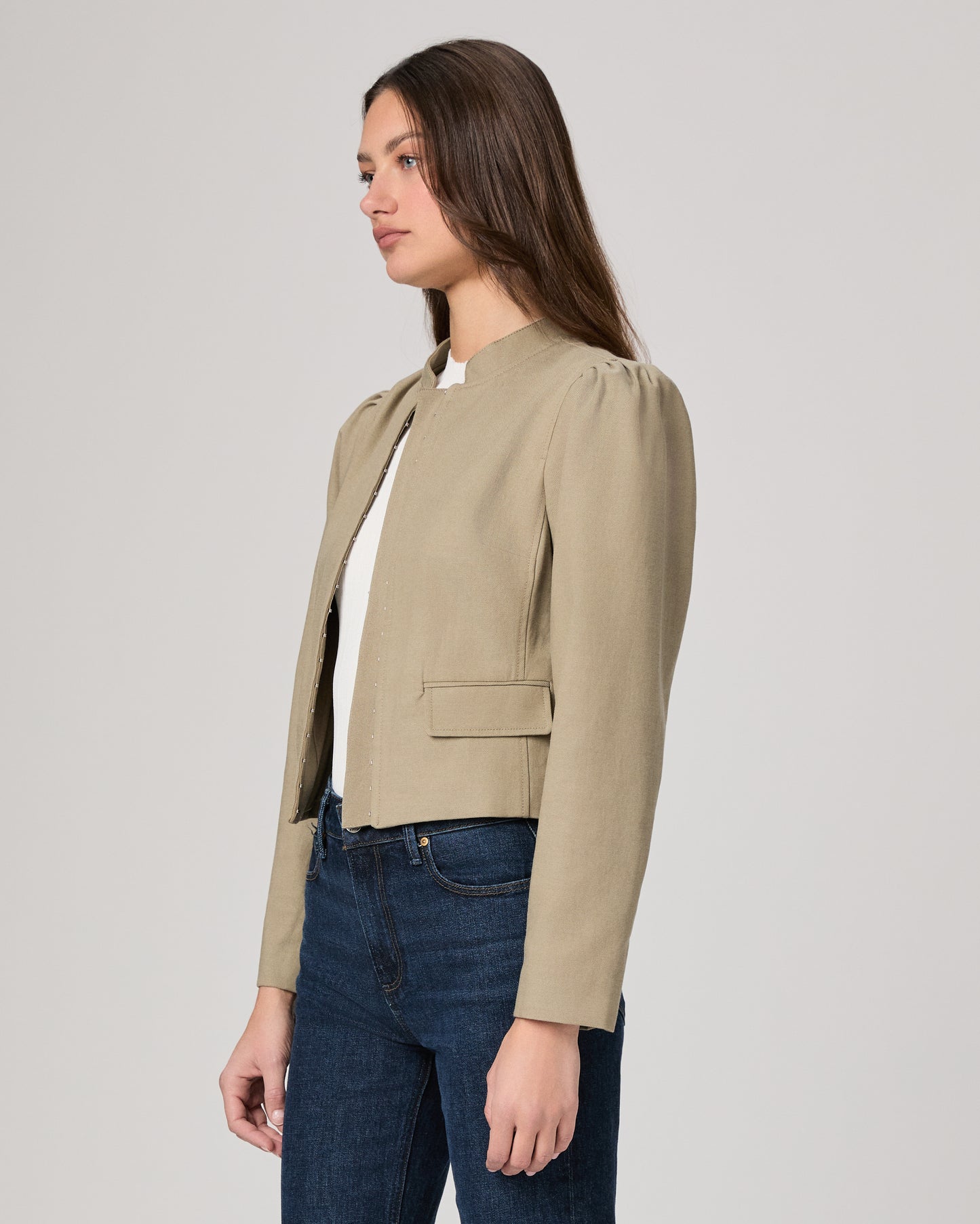 Woman wearing a light green jacket and dark blue jeans on a white background