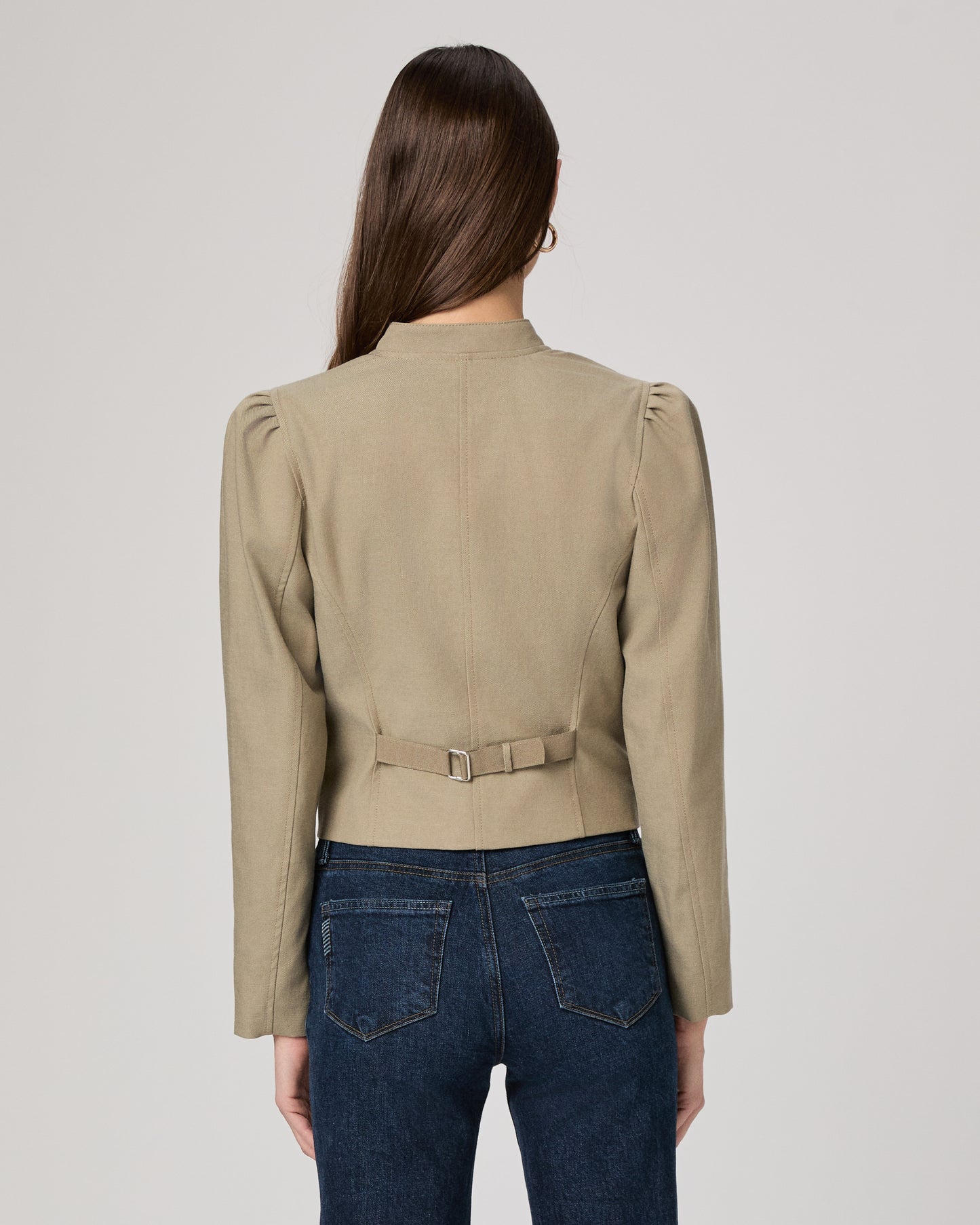 Woman wearing a light green jacket and dark blue jeans on a white background