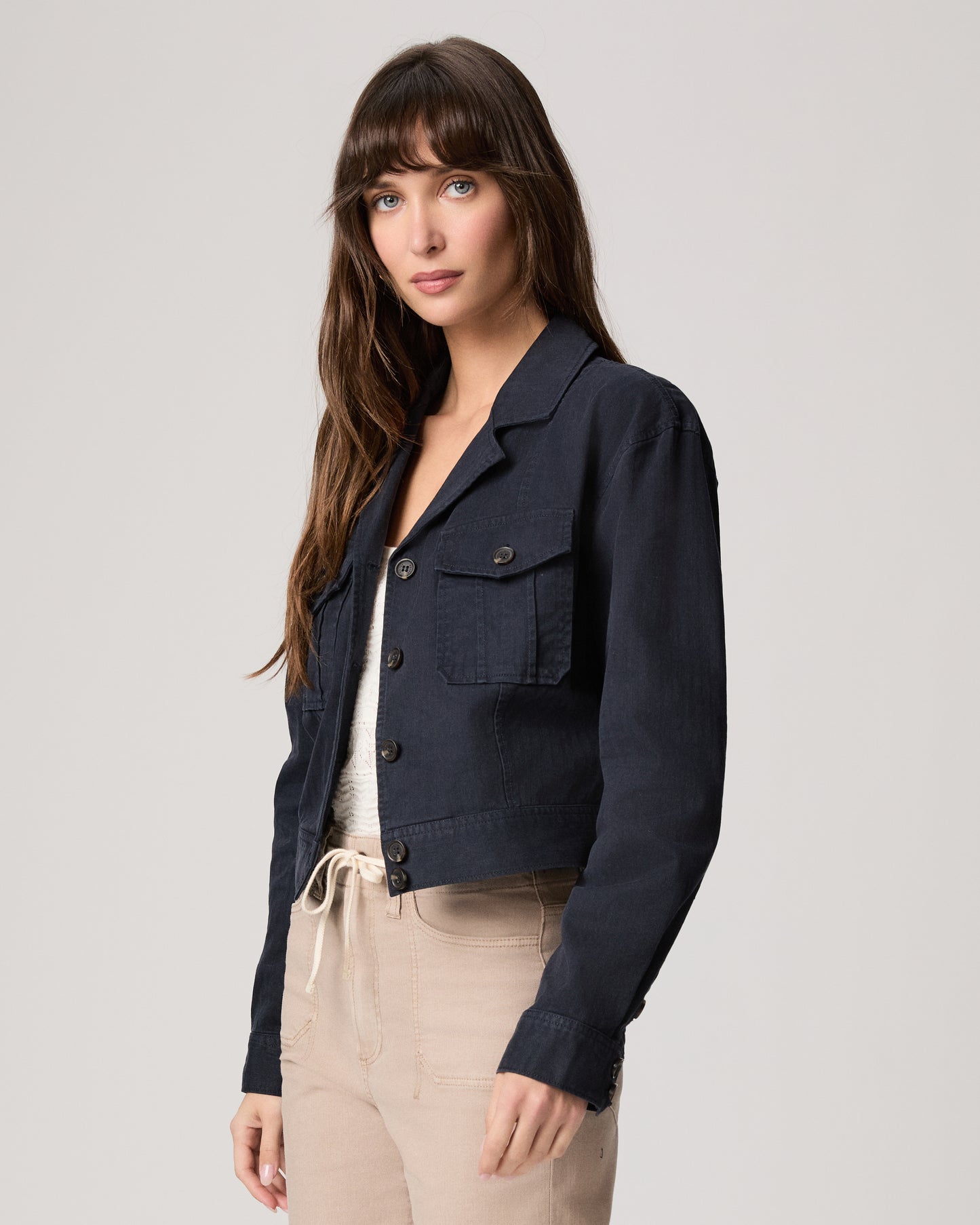Woman wearing a navy jacket over a white top and beige pants on a light gray background