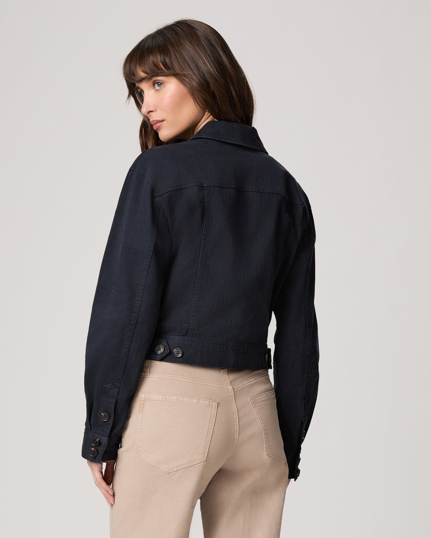 Woman wearing a navy jacket over a white top and beige pants on a light gray background