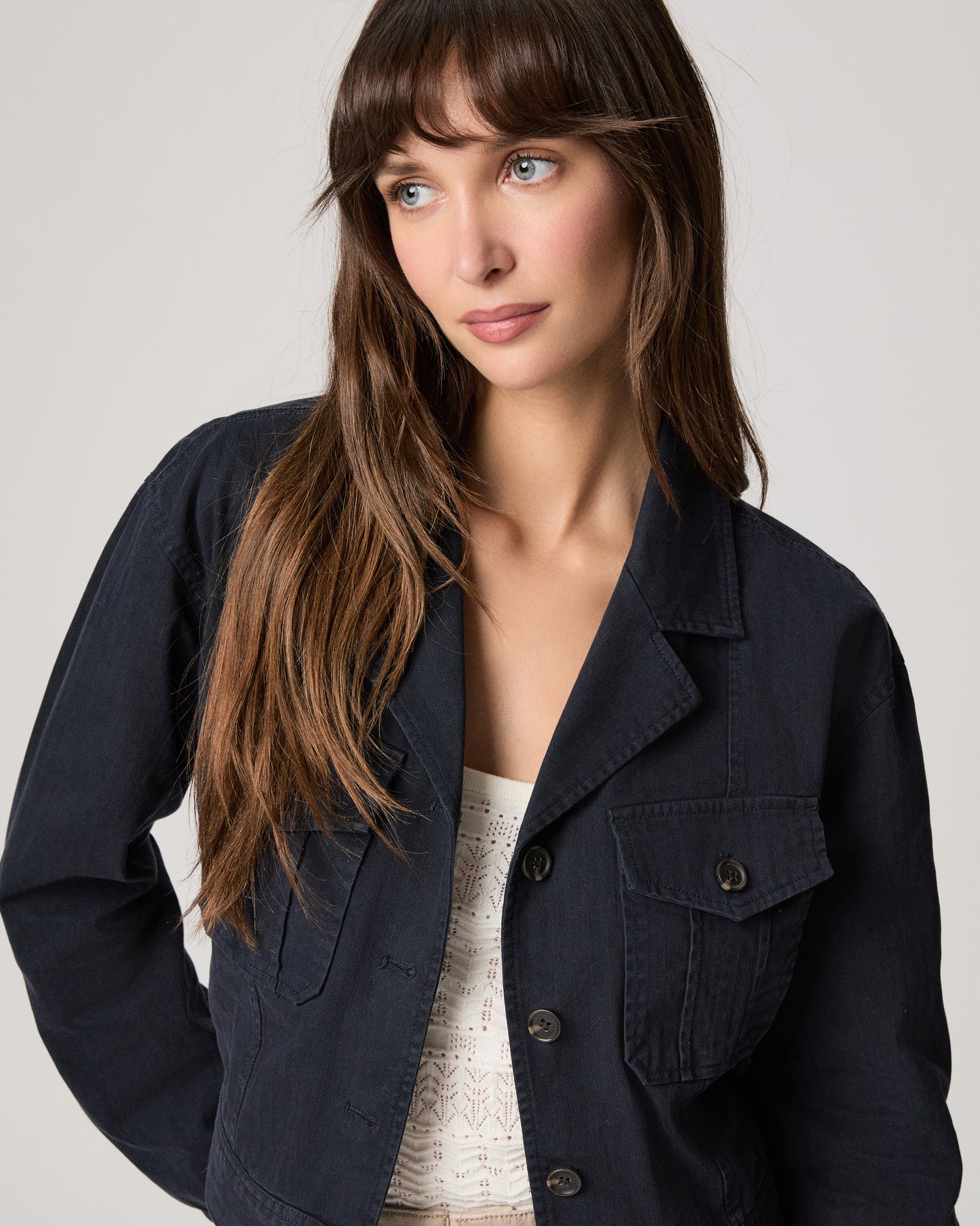 Woman wearing a navy jacket over a white top and beige pants on a light gray background