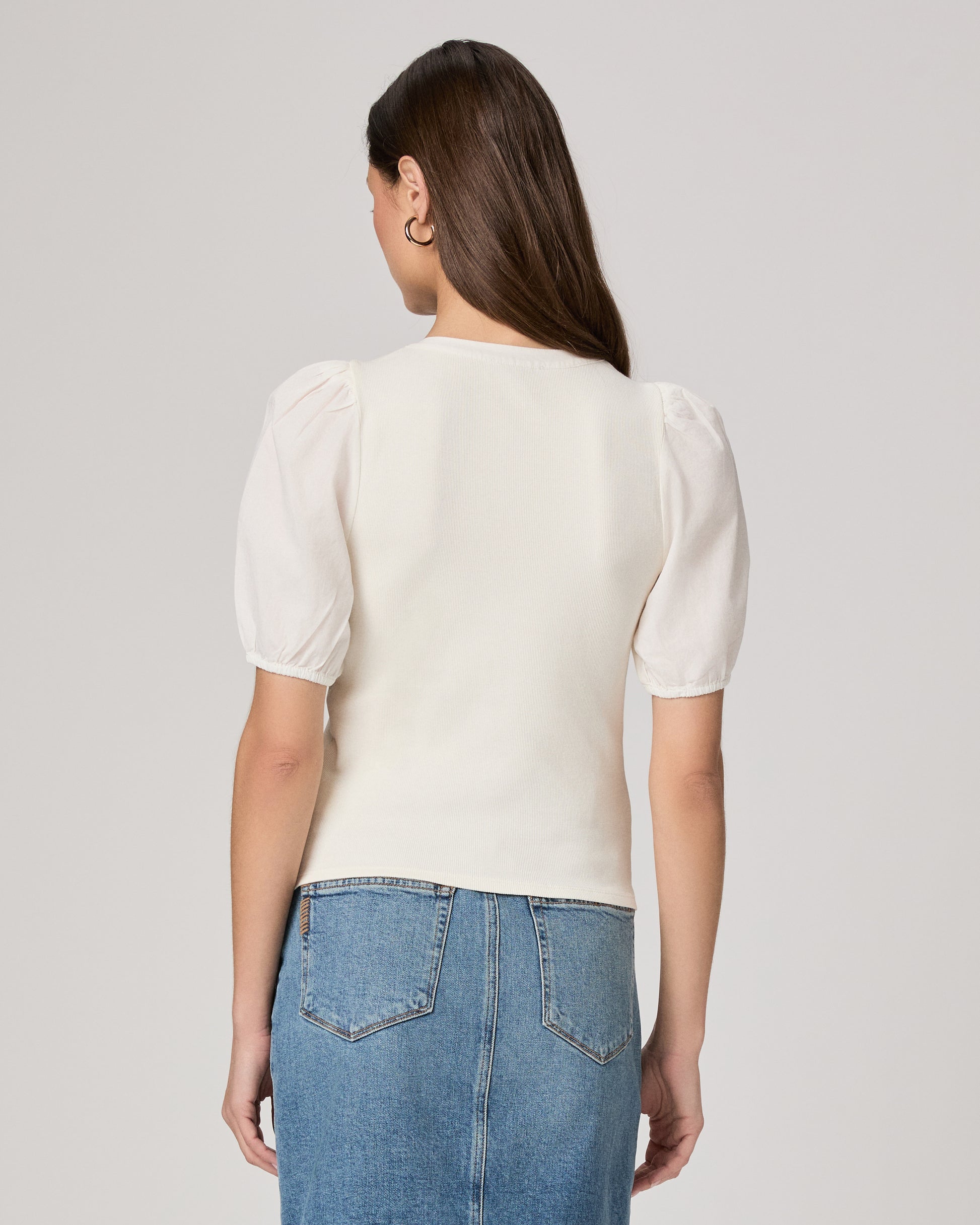 Woman wearing a white blouse and blue denim skirt paired with brown belt on a plain background