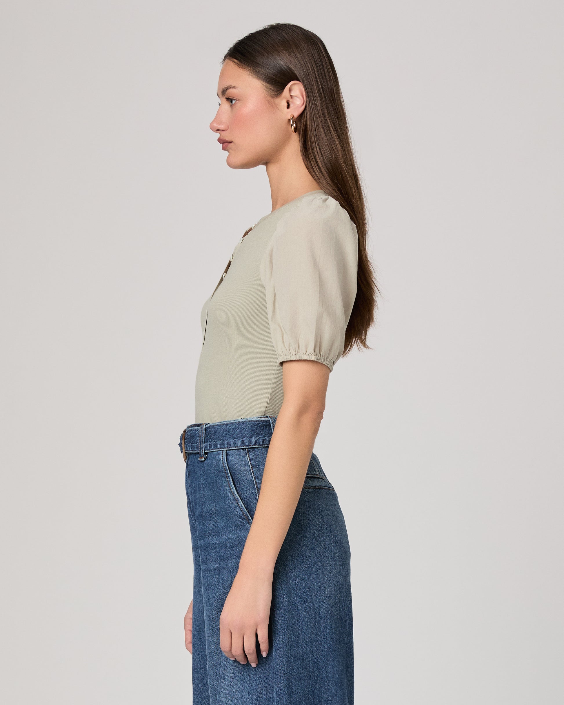 Woman wearing a light green blouse with puffed sleeves and blue jeans on a plain background