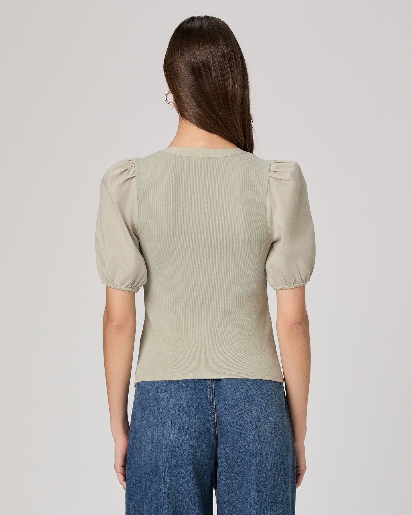 Woman wearing a light green blouse with puffed sleeves and blue jeans on a plain background