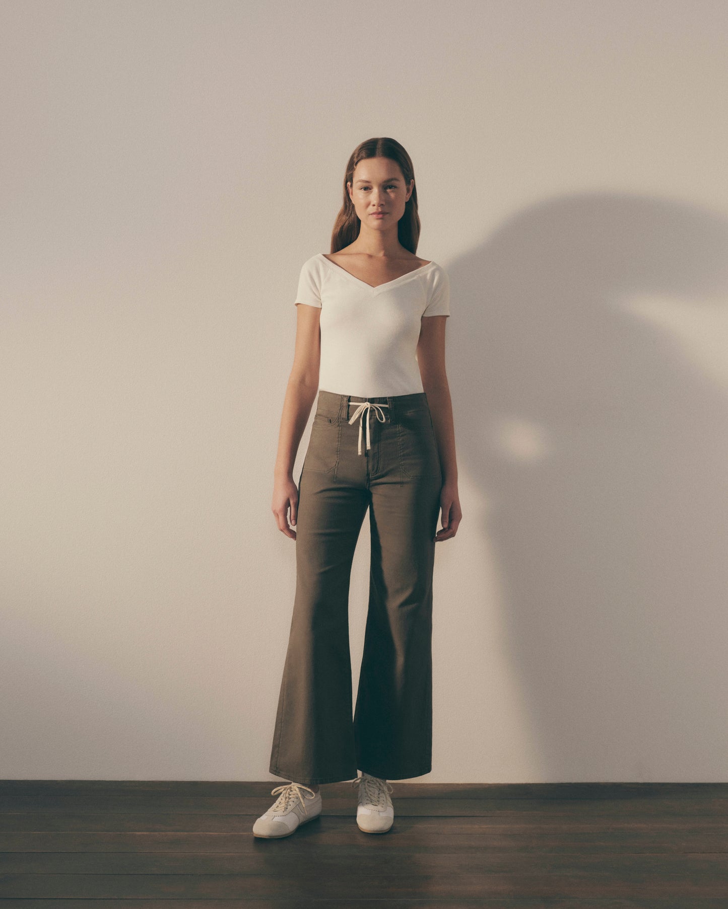 Woman wearing a white top and dark pants against a plain background