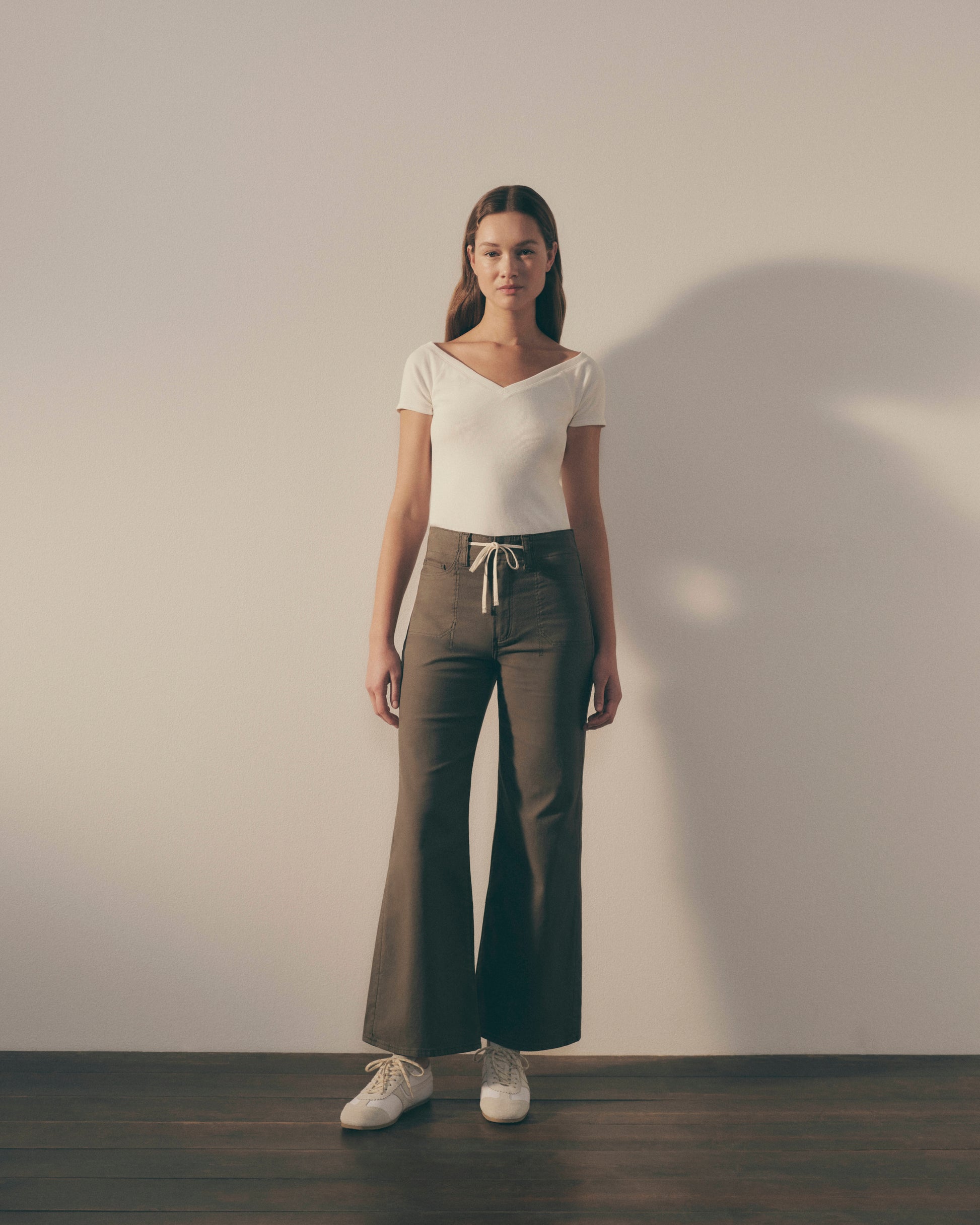 Woman wearing a white top and dark pants against a plain background