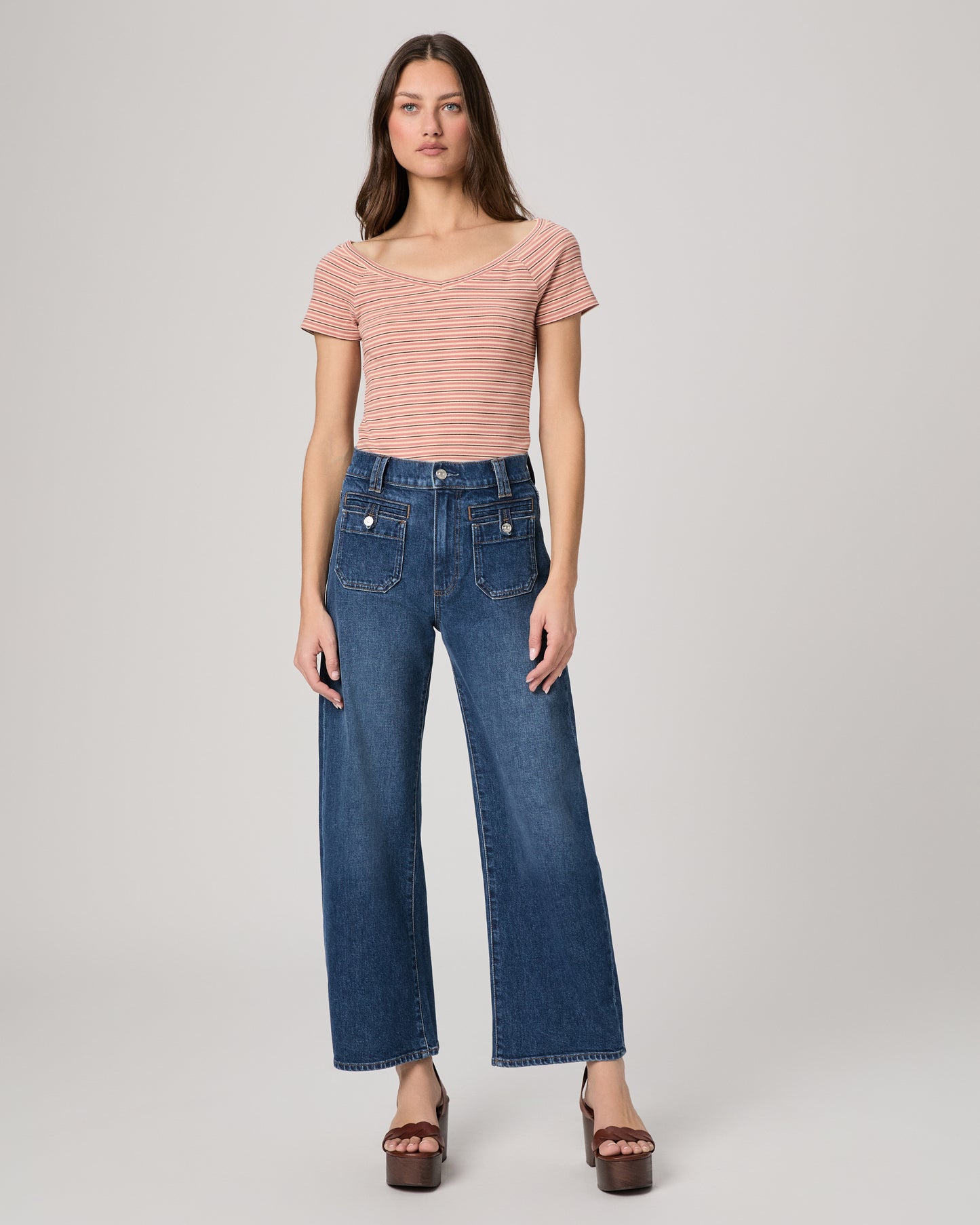 Woman wearing a striped pink top and blue jeans on a plain background