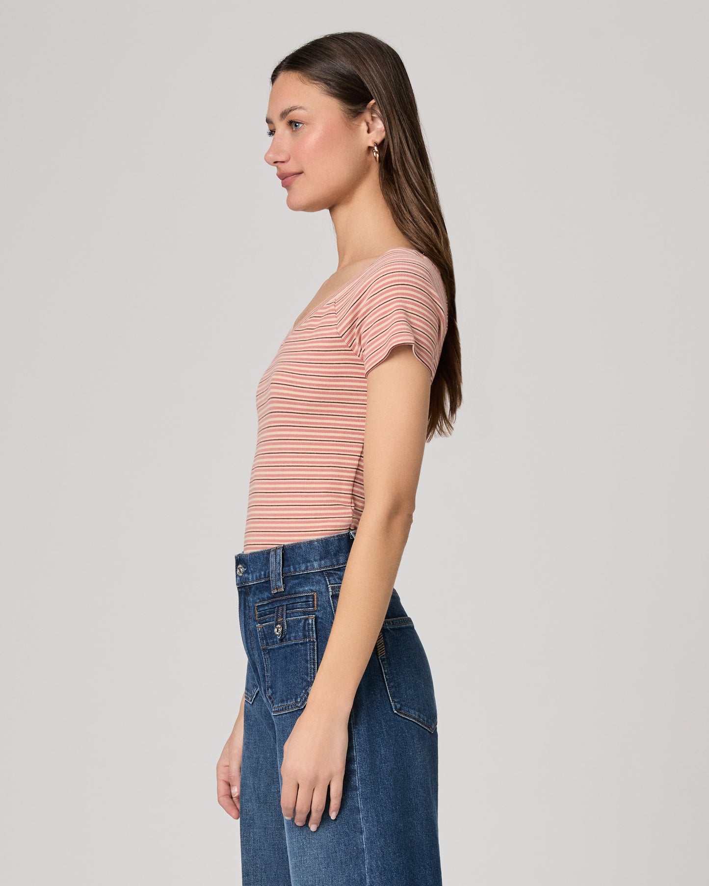Woman wearing a striped pink top and blue jeans on a plain background