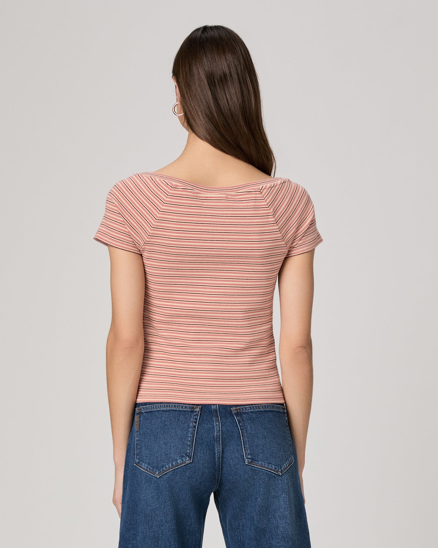 Woman wearing a striped pink top and blue jeans on a plain background
