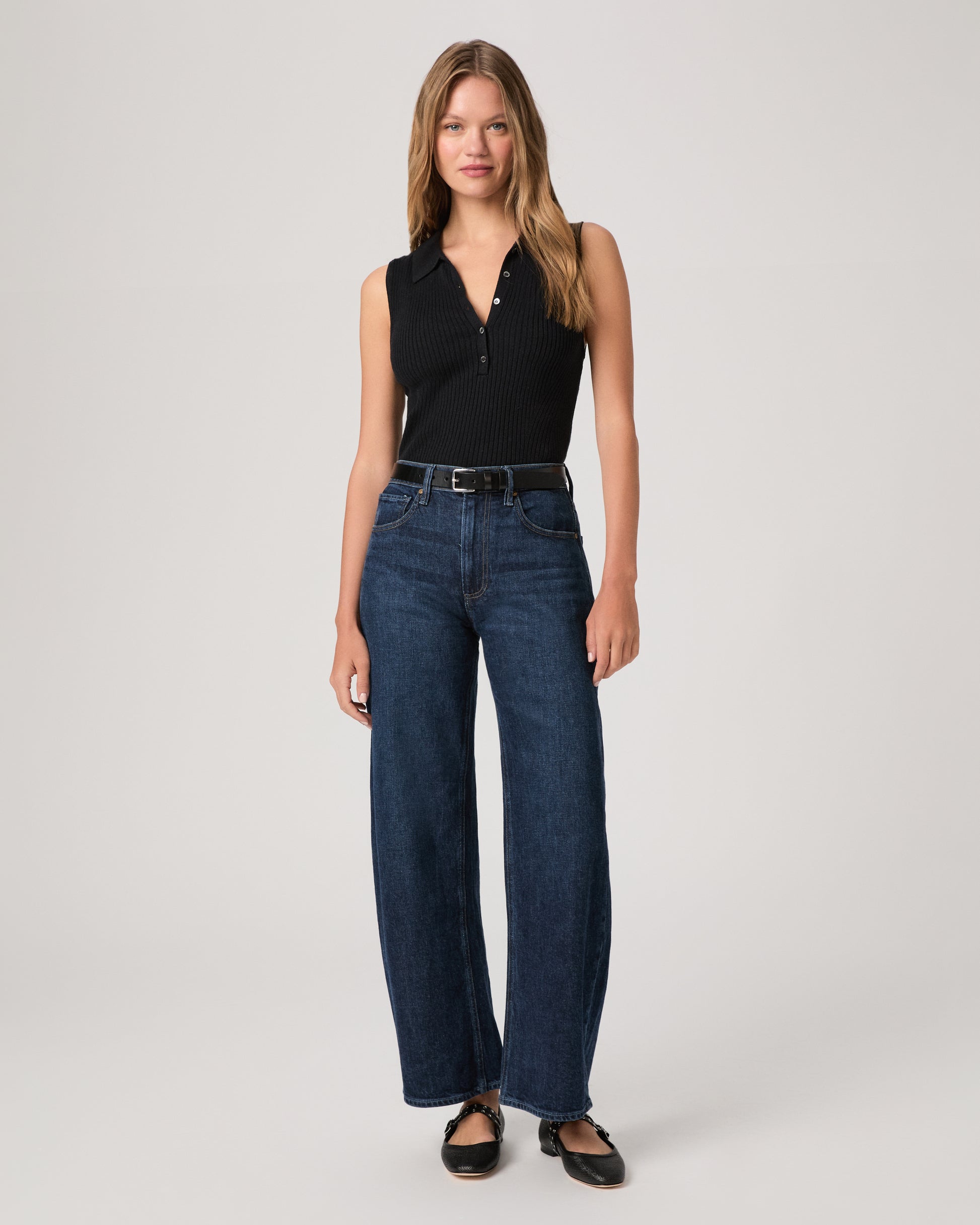 Woman wearing a black sleeveless top and blue jeans on a white background