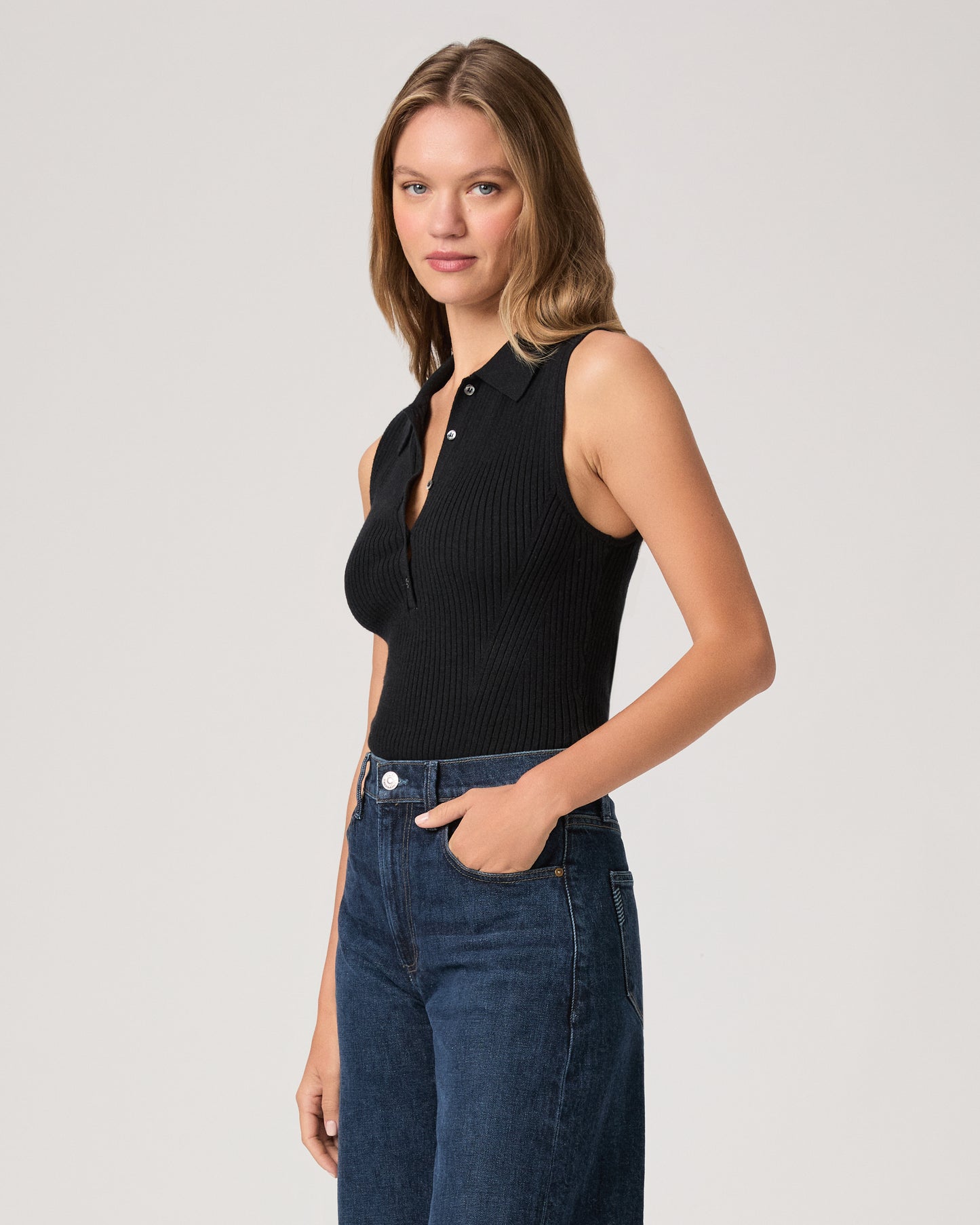 Woman wearing a black sleeveless top and blue jeans on a plain background