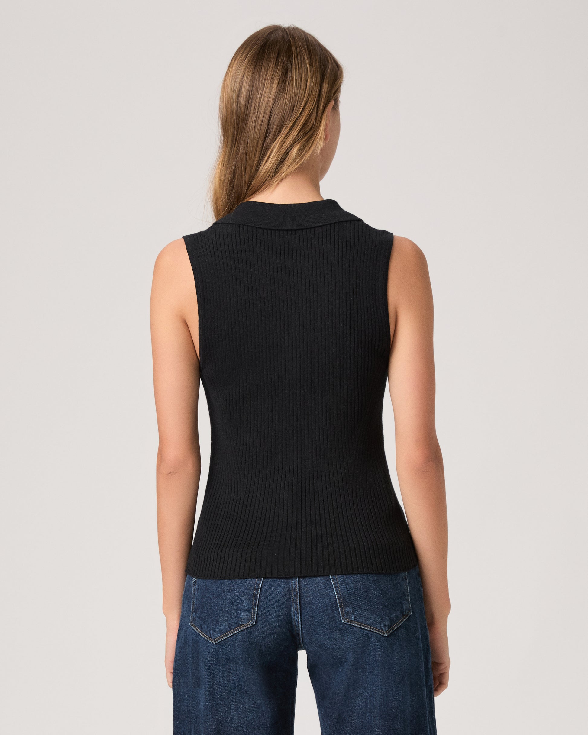 Person wearing a black sleeveless ribbed top and blue jeans on a light gray background