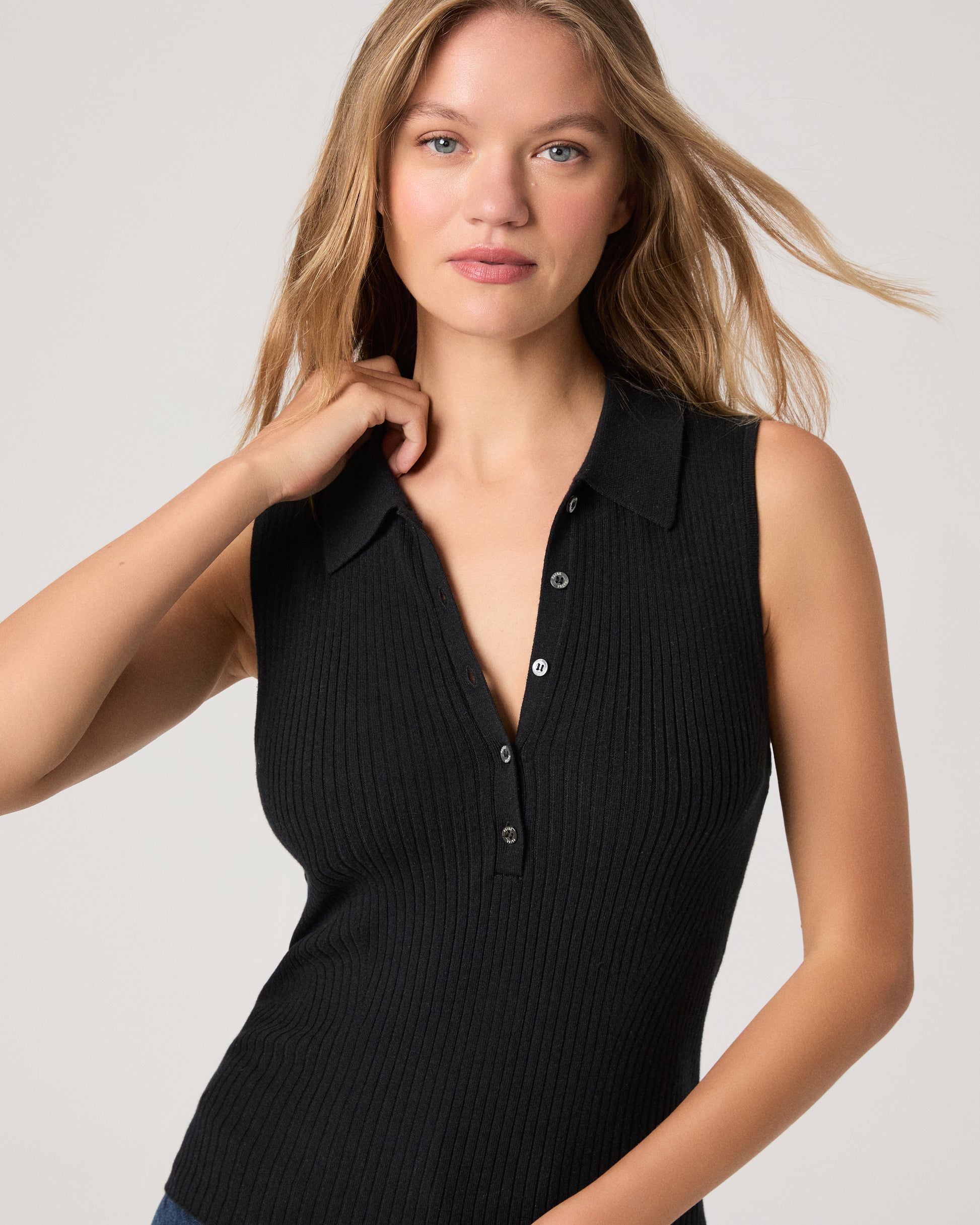 Woman wearing a black sleeveless dress with buttons on a light gray background