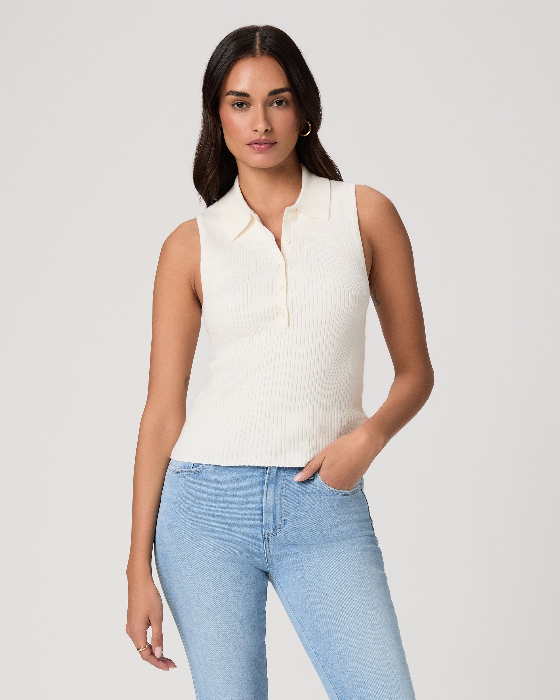 Woman wearing a white sleeveless shirt and light jeans against a white background