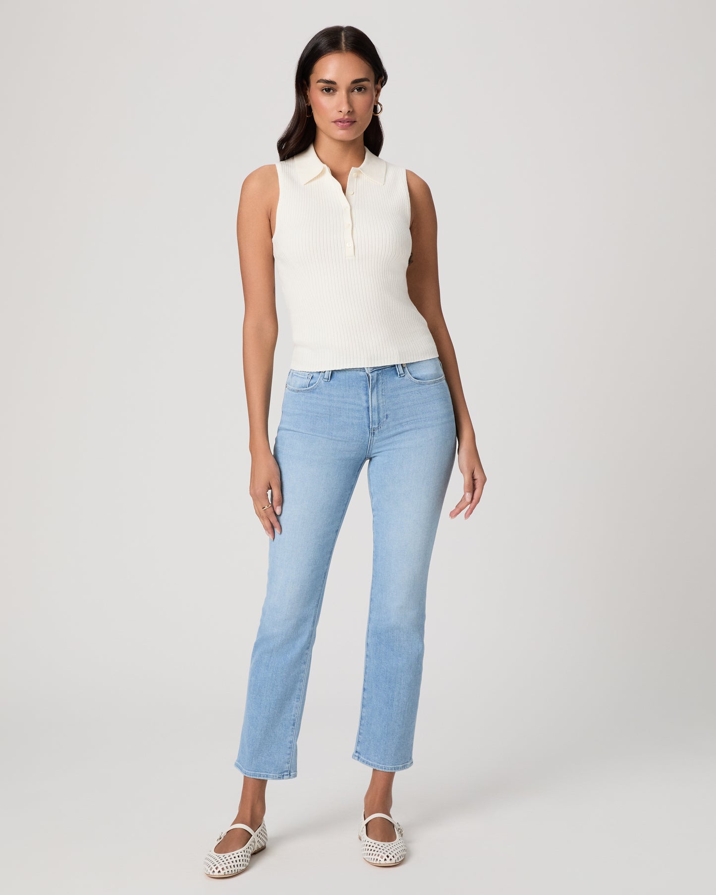 Woman wearing a white sleeveless shirt and light jeans against a white background