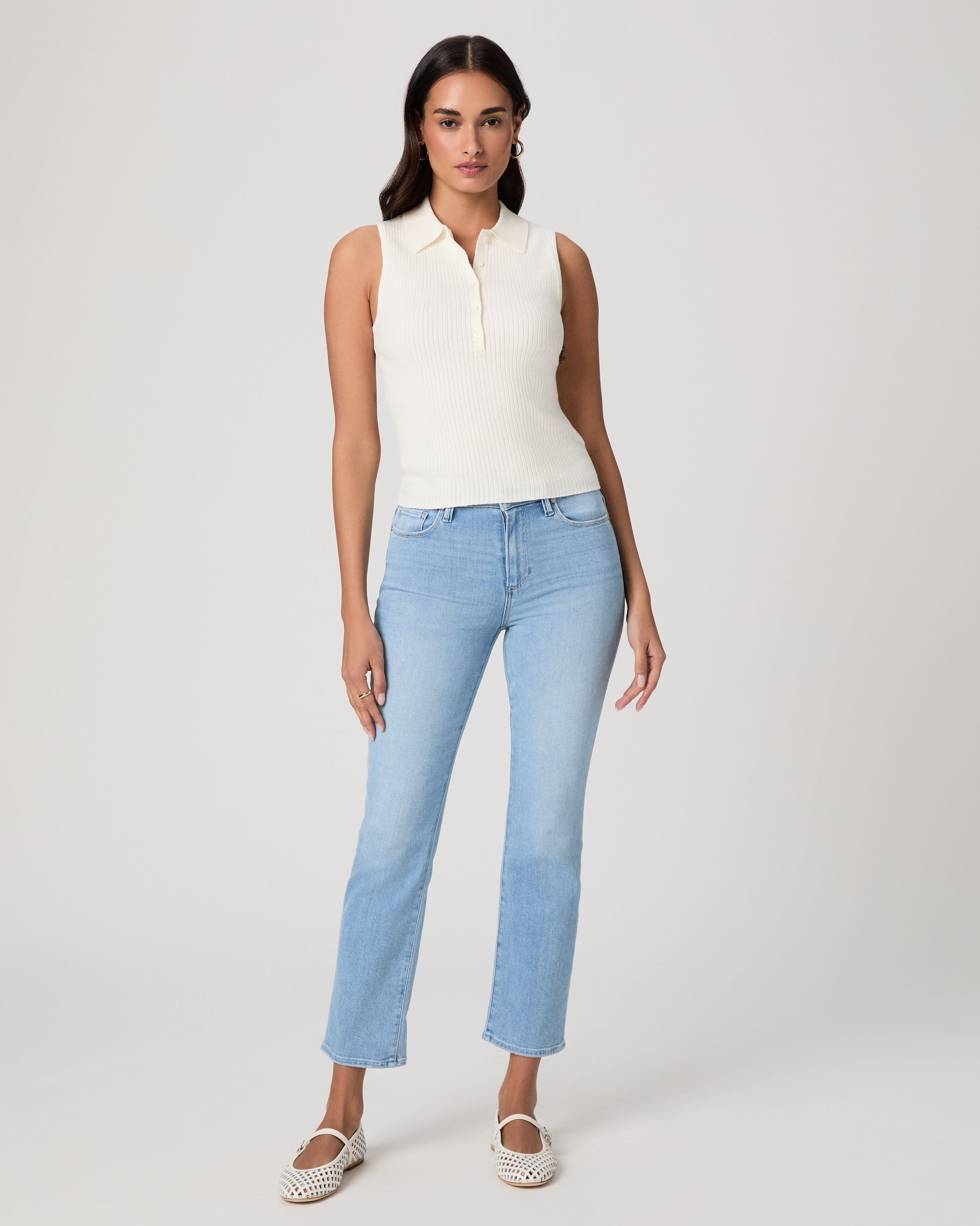 Woman wearing a white sleeveless shirt and light jeans against a white background