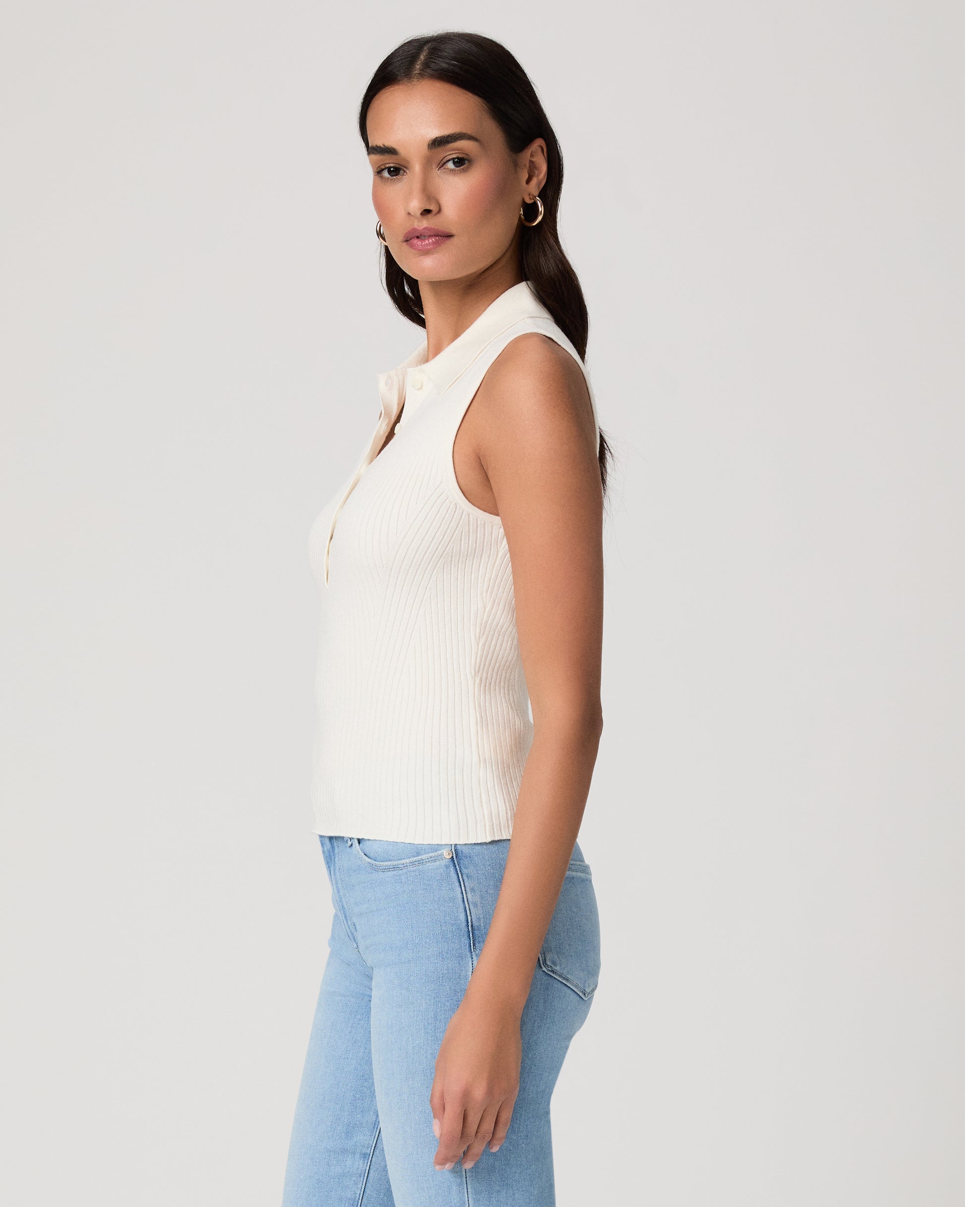 Woman wearing a white sleeveless shirt and light jeans against a white background