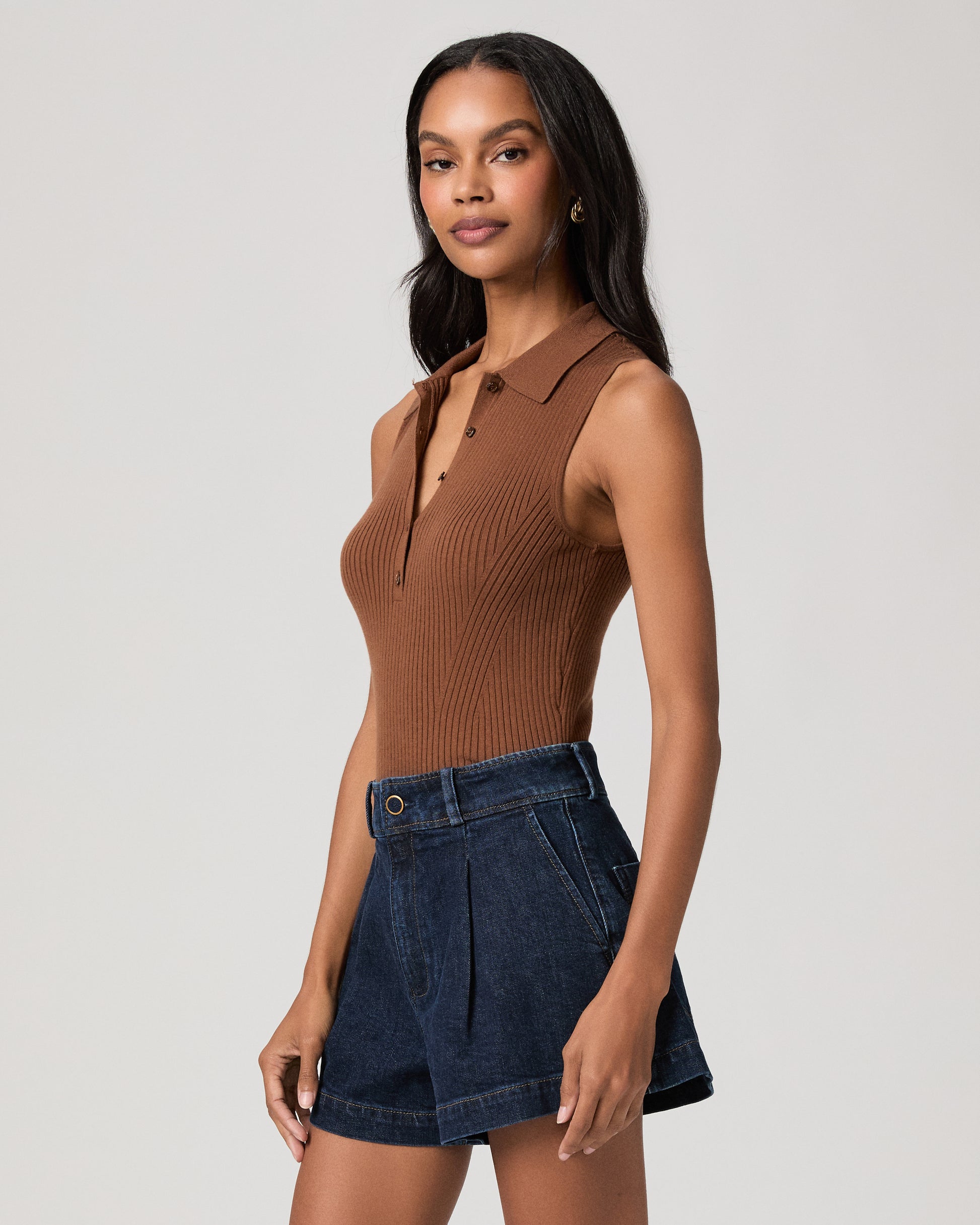 Woman wearing a textured brown top and dark blue shorts on a white background