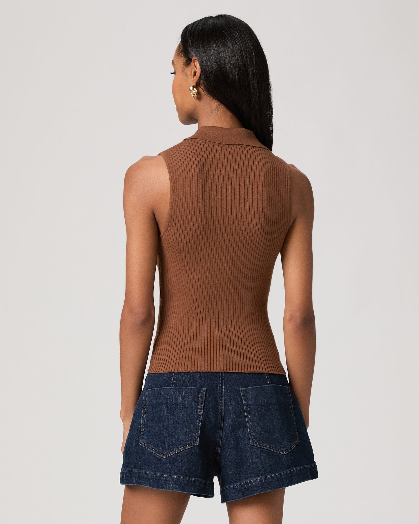 Woman wearing a textured brown top and dark blue shorts on a white background