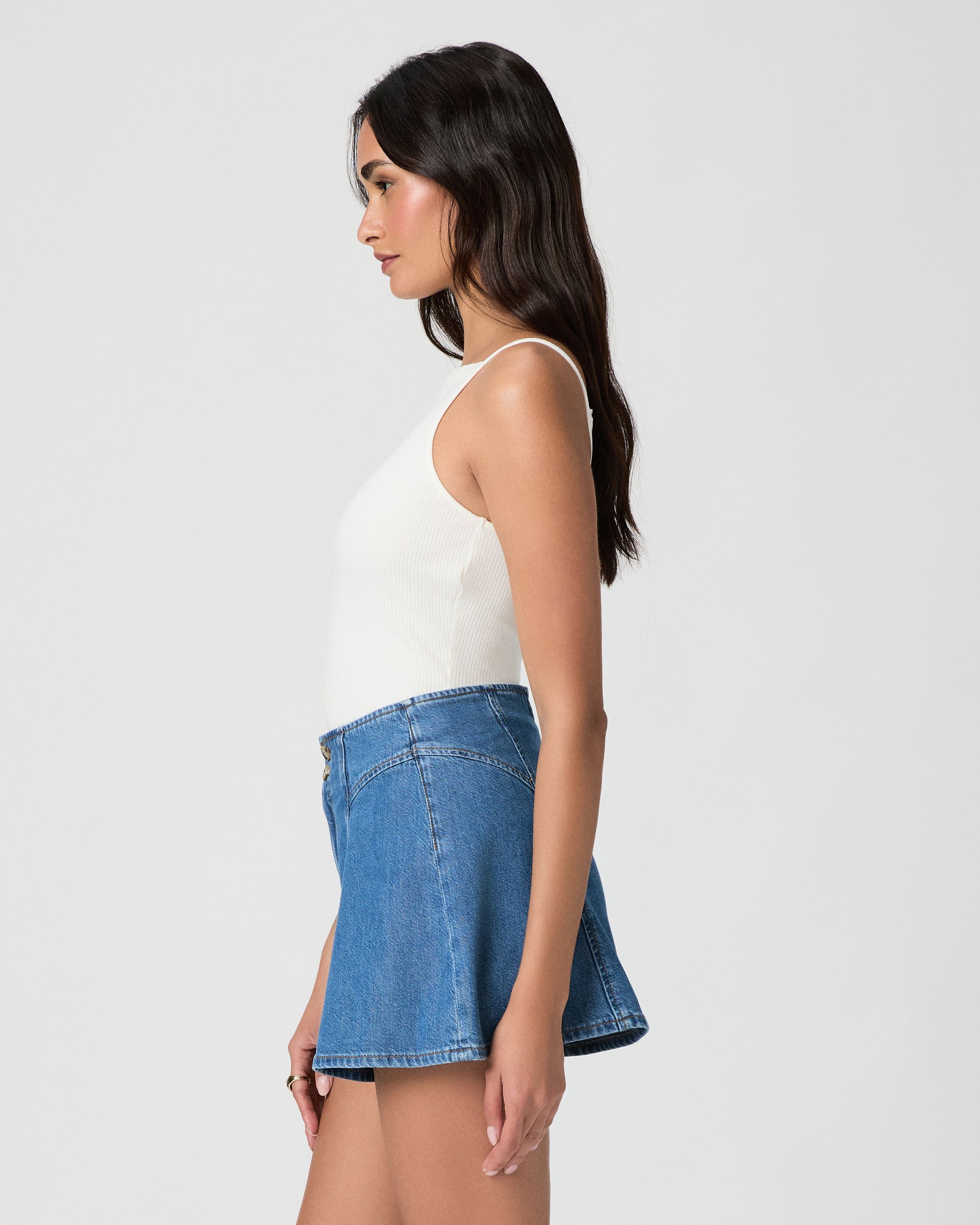 Woman wearing a white tank top and blue denim shorts on a plain background