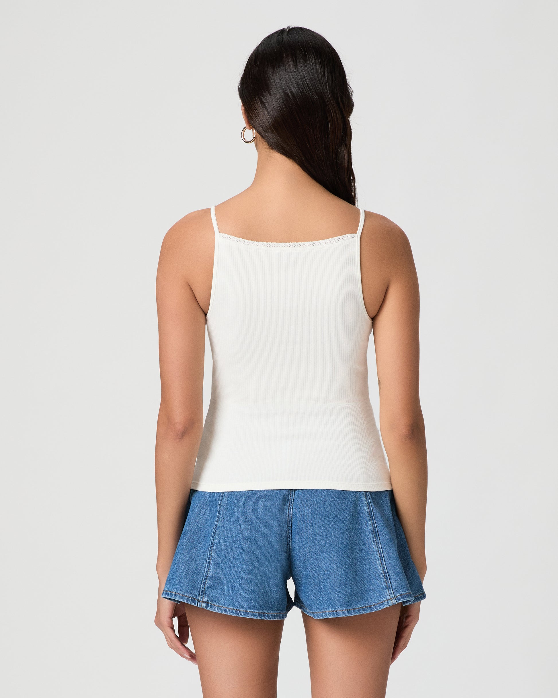 Woman wearing a white tank top and blue denim shorts on a plain background