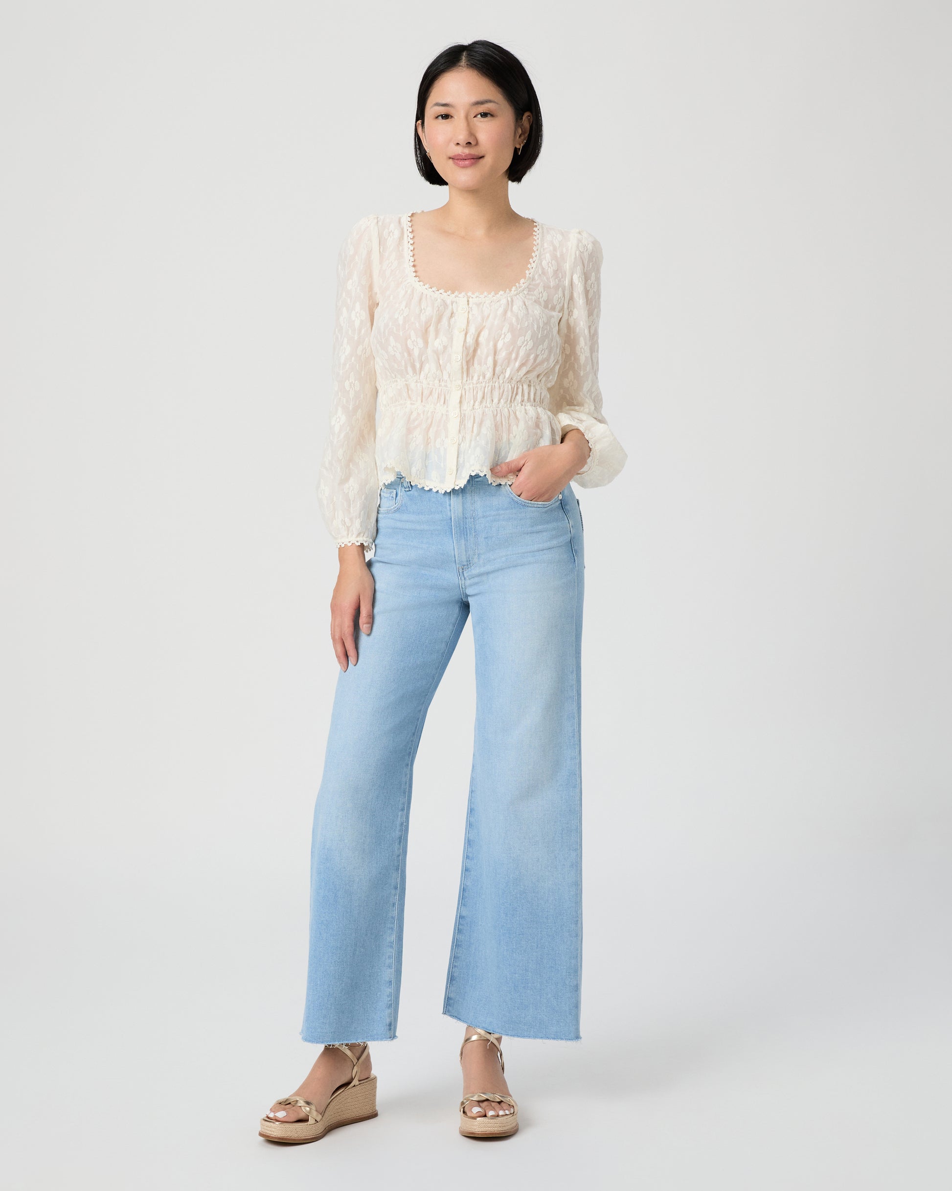Woman wearing a white blouse and light blue jeans paired with gold wedges on a white background