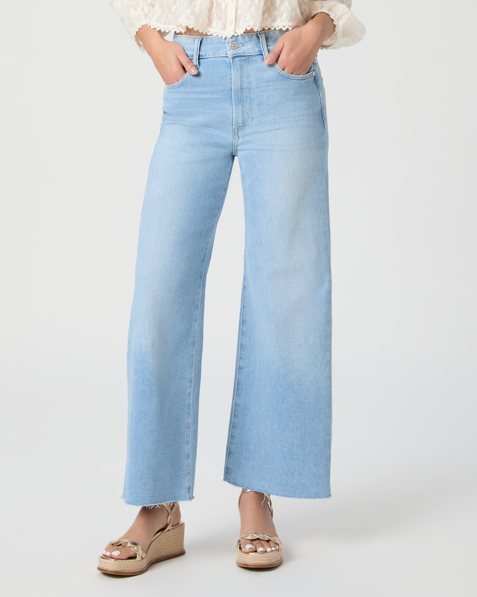 Woman wearing a white blouse and light blue jeans paired with gold wedges on a white background