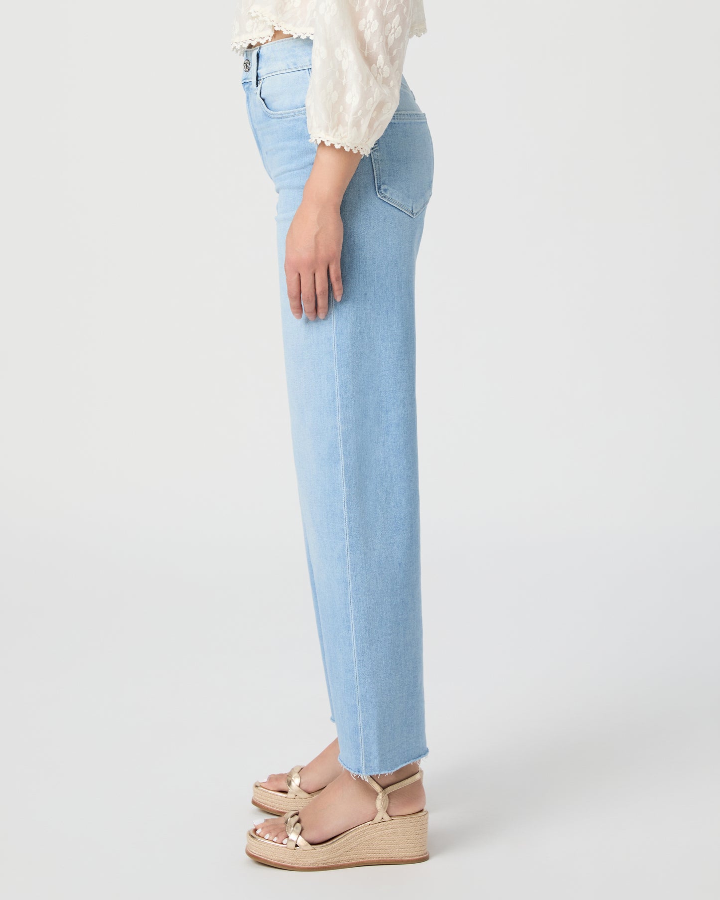 Woman wearing a white blouse and light blue jeans paired with gold wedges on a white background