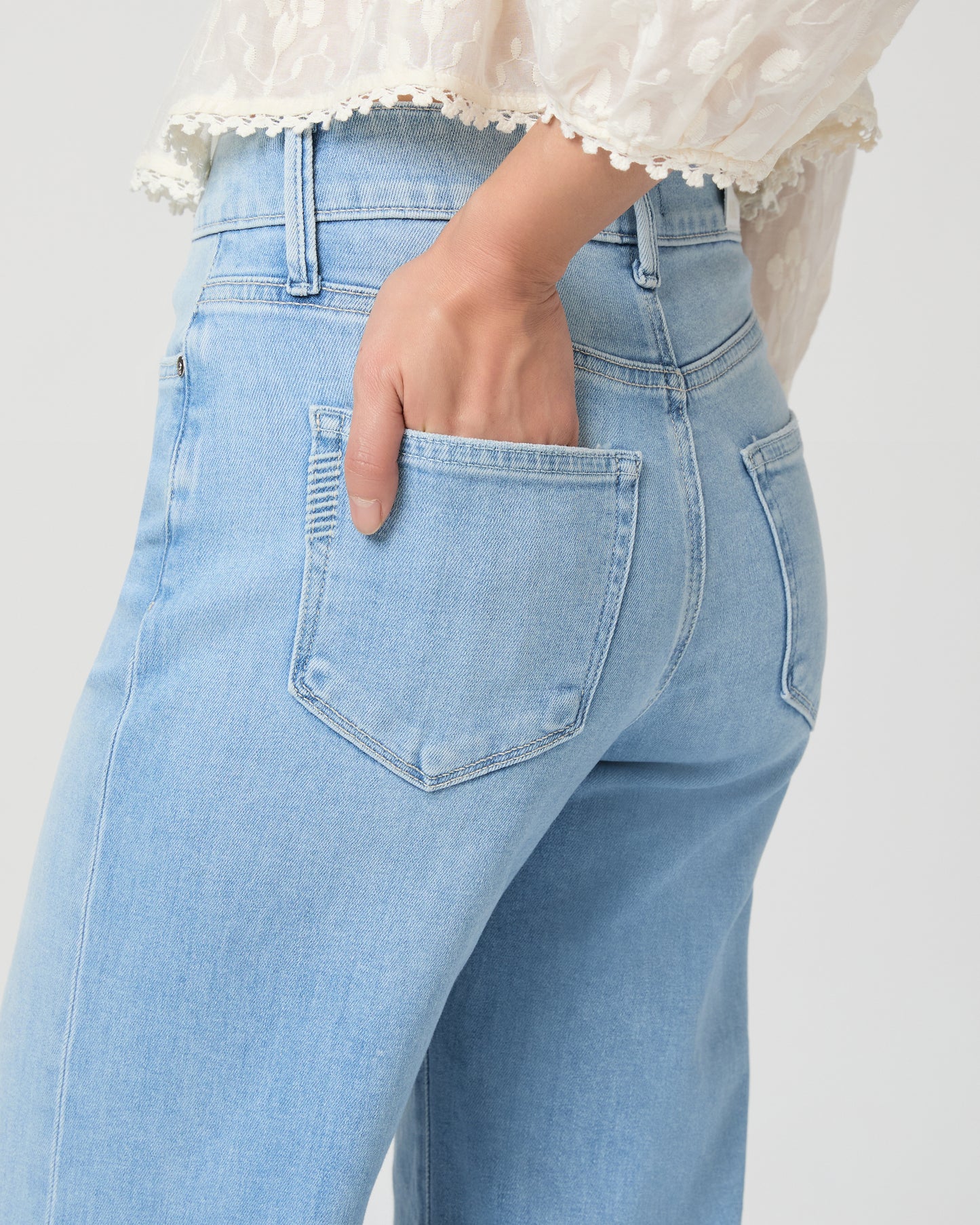 Woman wearing a white blouse and light blue jeans paired with gold wedges on a white background