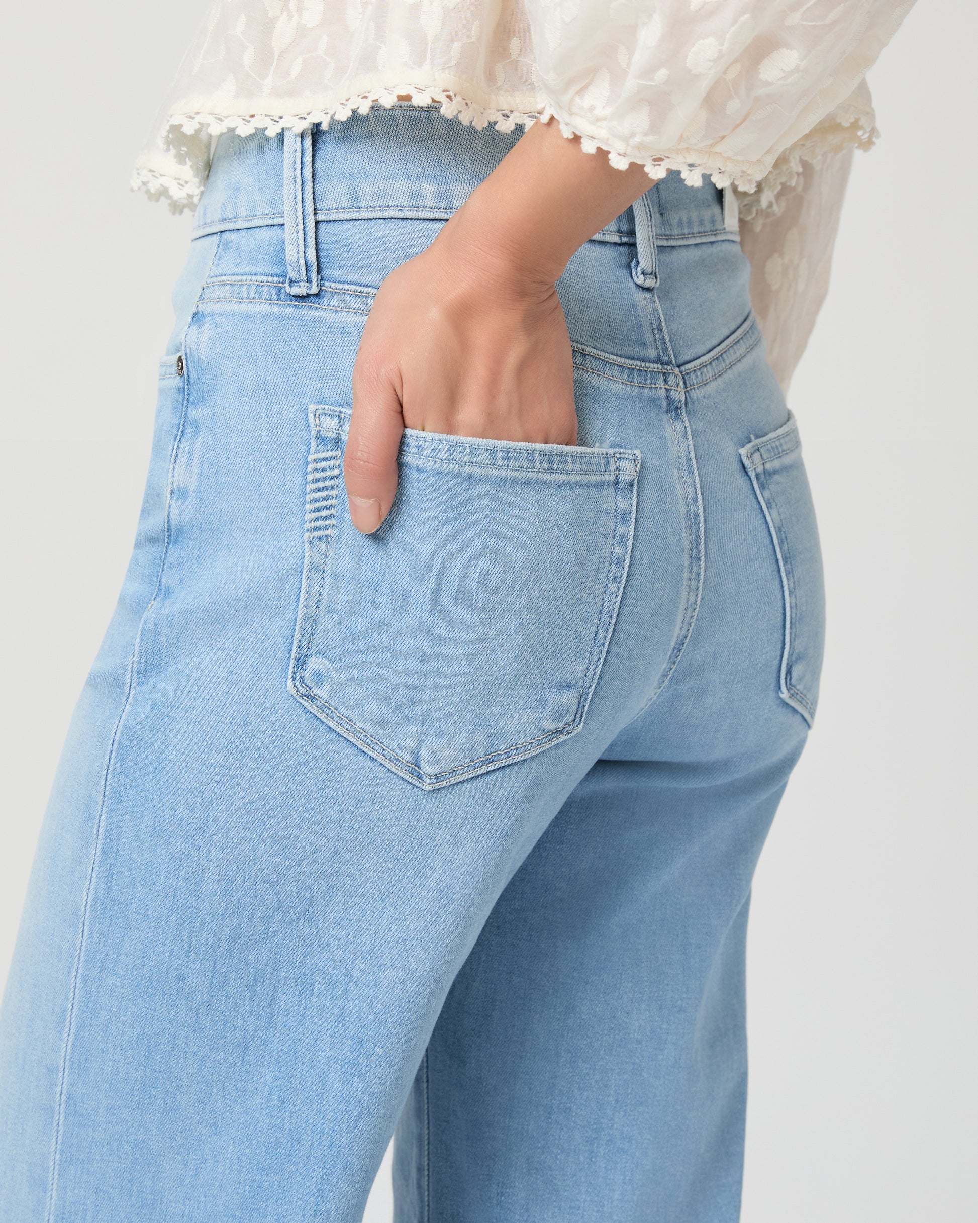 Woman wearing a white blouse and light blue jeans paired with gold wedges on a white background