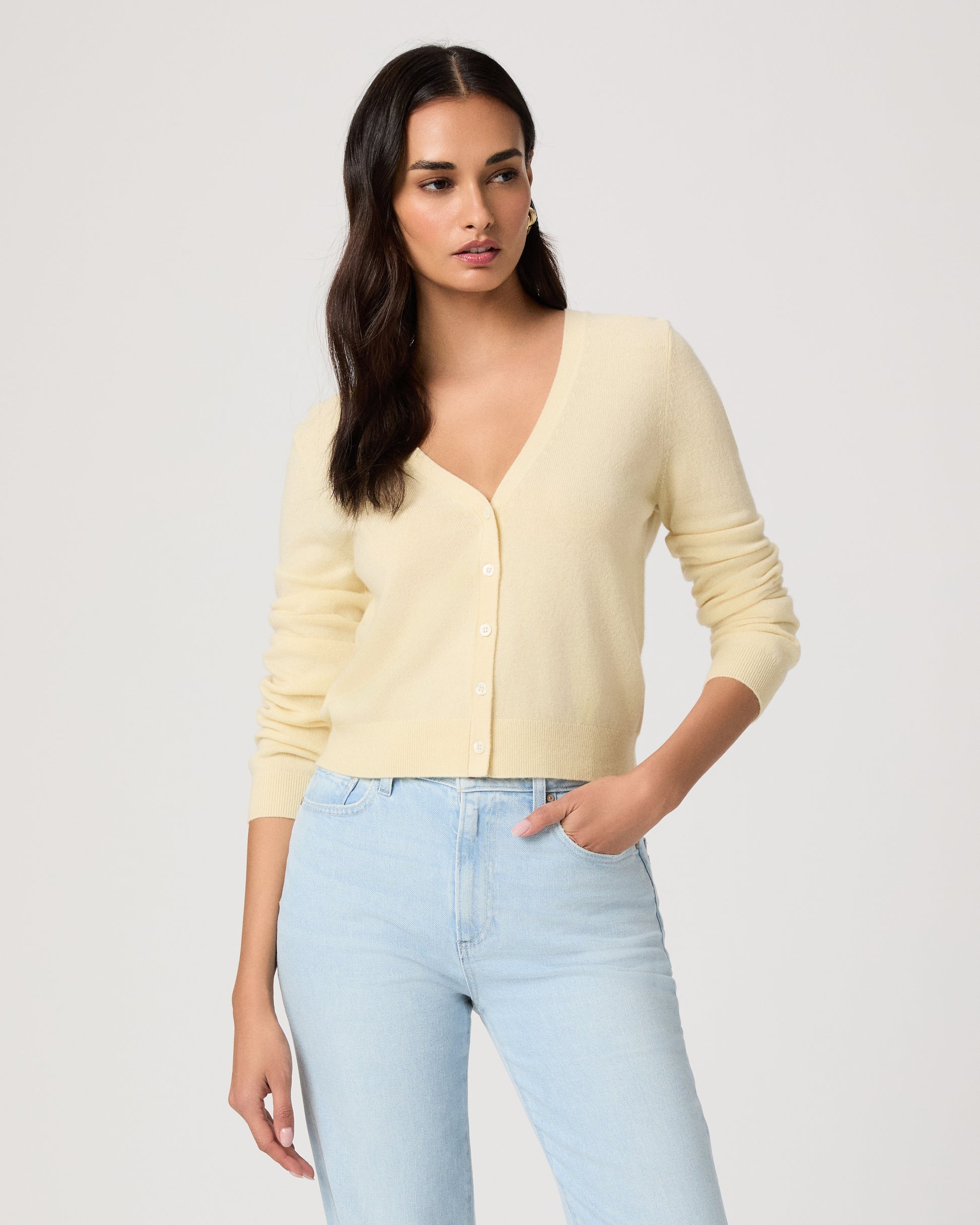 Woman wearing a light yellow cardigan and light blue jeans on a white background