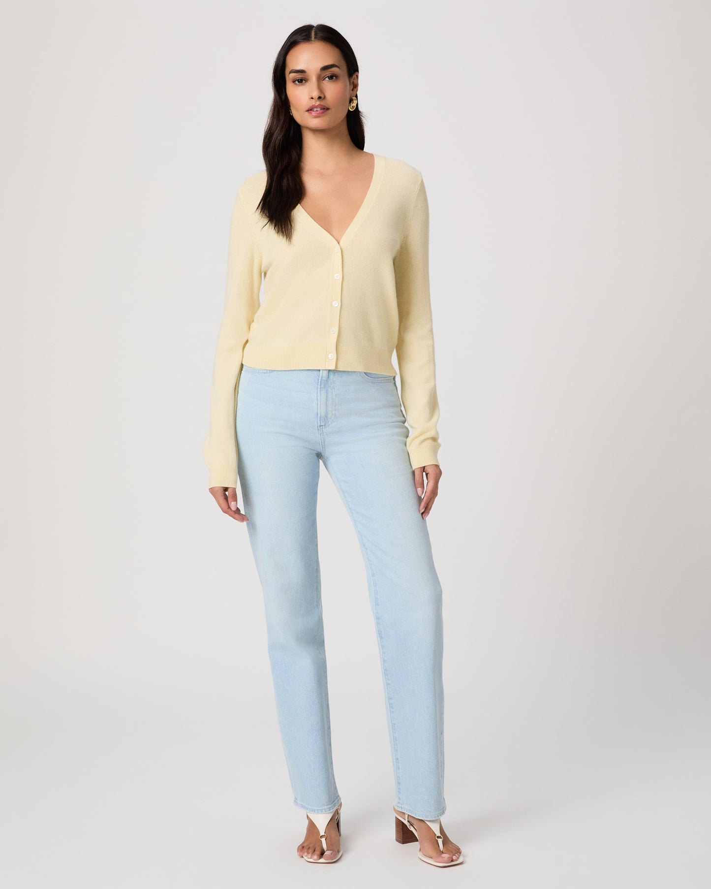 Woman wearing a light yellow cardigan and light blue jeans on a white background