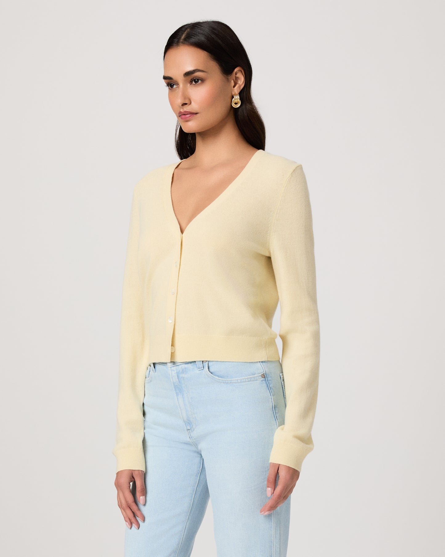 Woman wearing a light yellow cardigan and light blue jeans on a white background