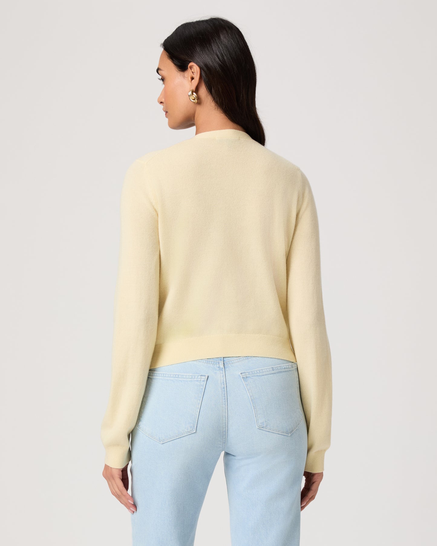 Woman wearing a light yellow cardigan and light blue jeans on a white background
