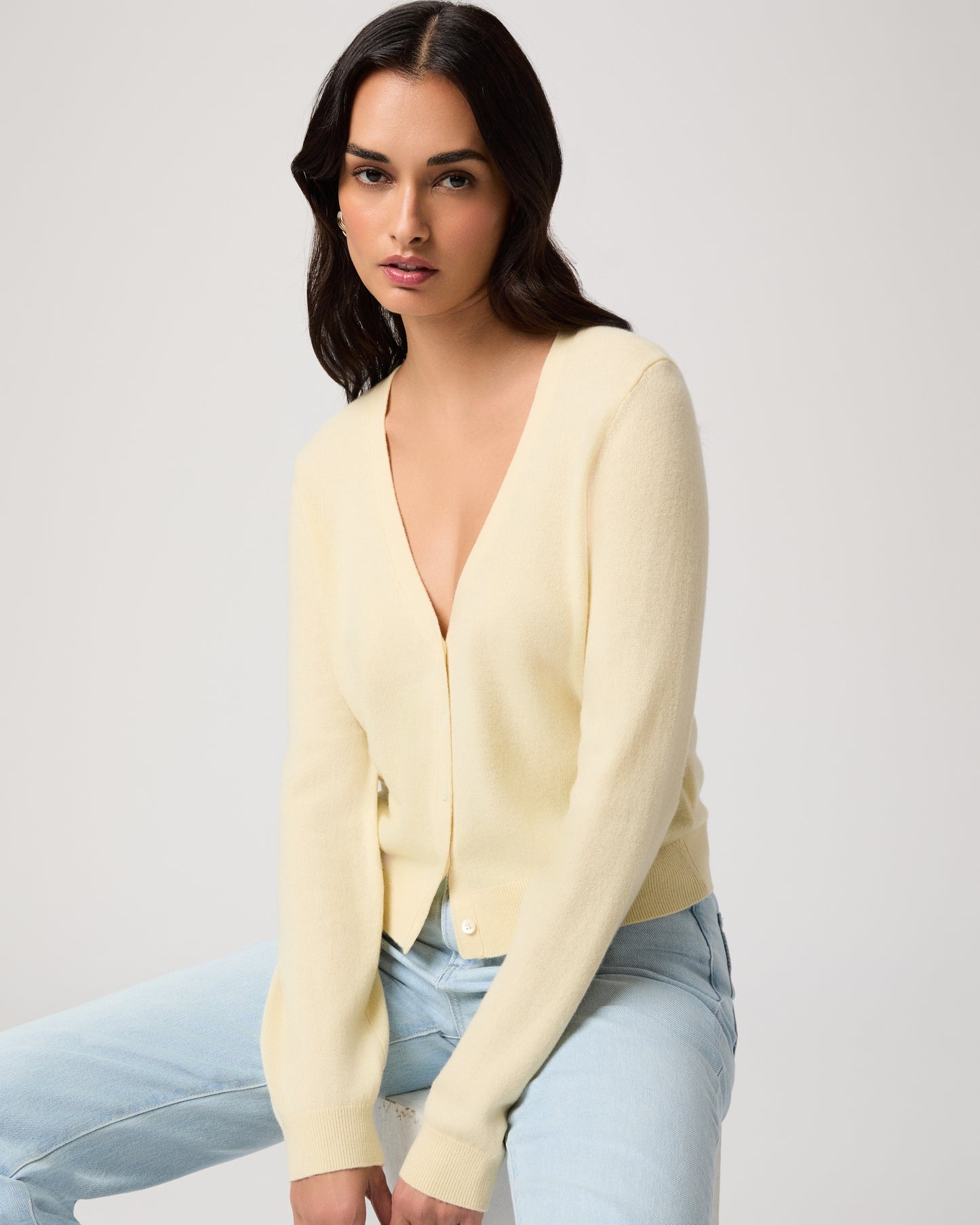 Woman wearing a light yellow cardigan and light blue jeans on a white background