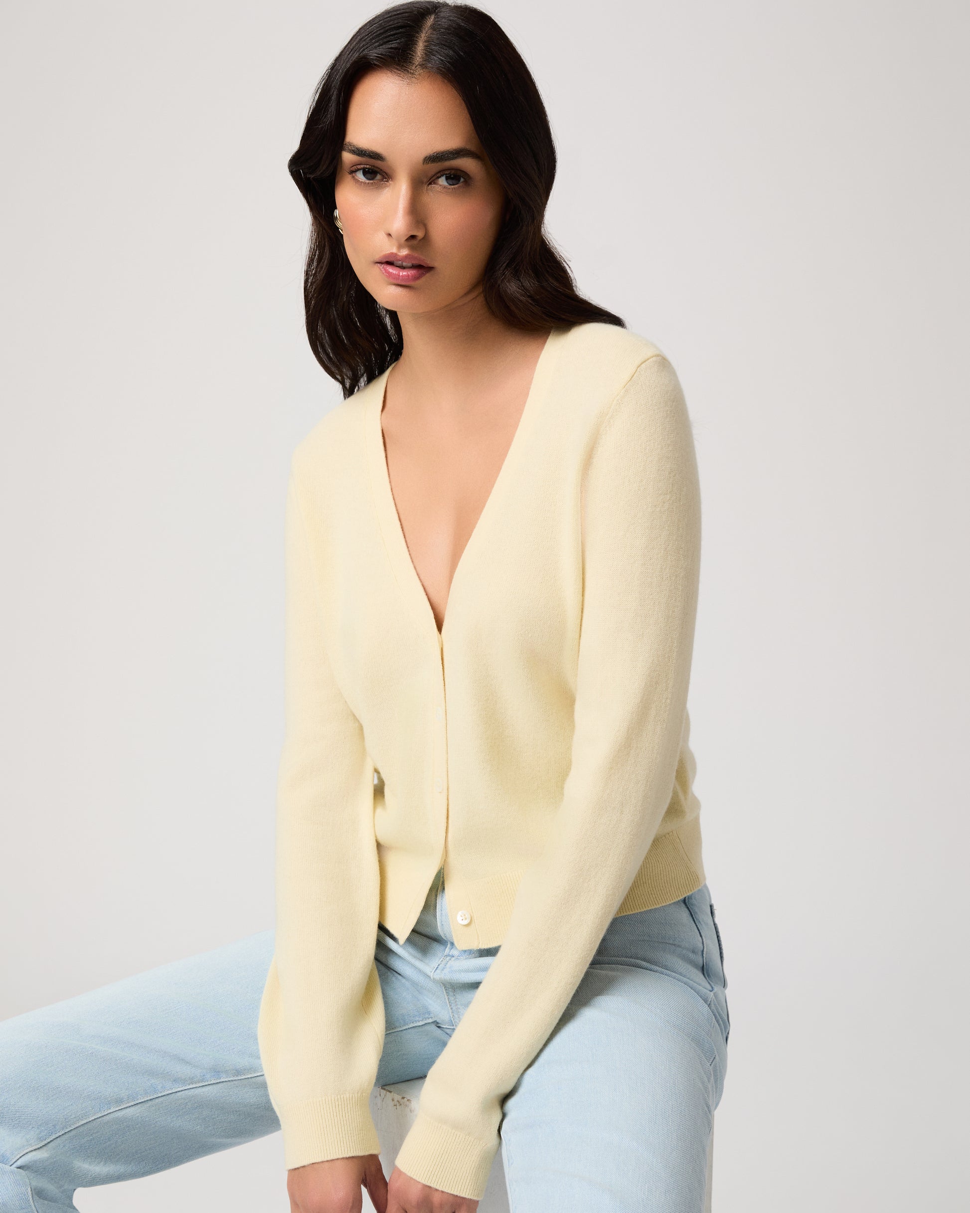 Woman wearing a light yellow cardigan and light blue jeans on a white background
