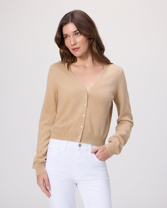 Woman wearing a beige cardigan and white pants on a light gray background