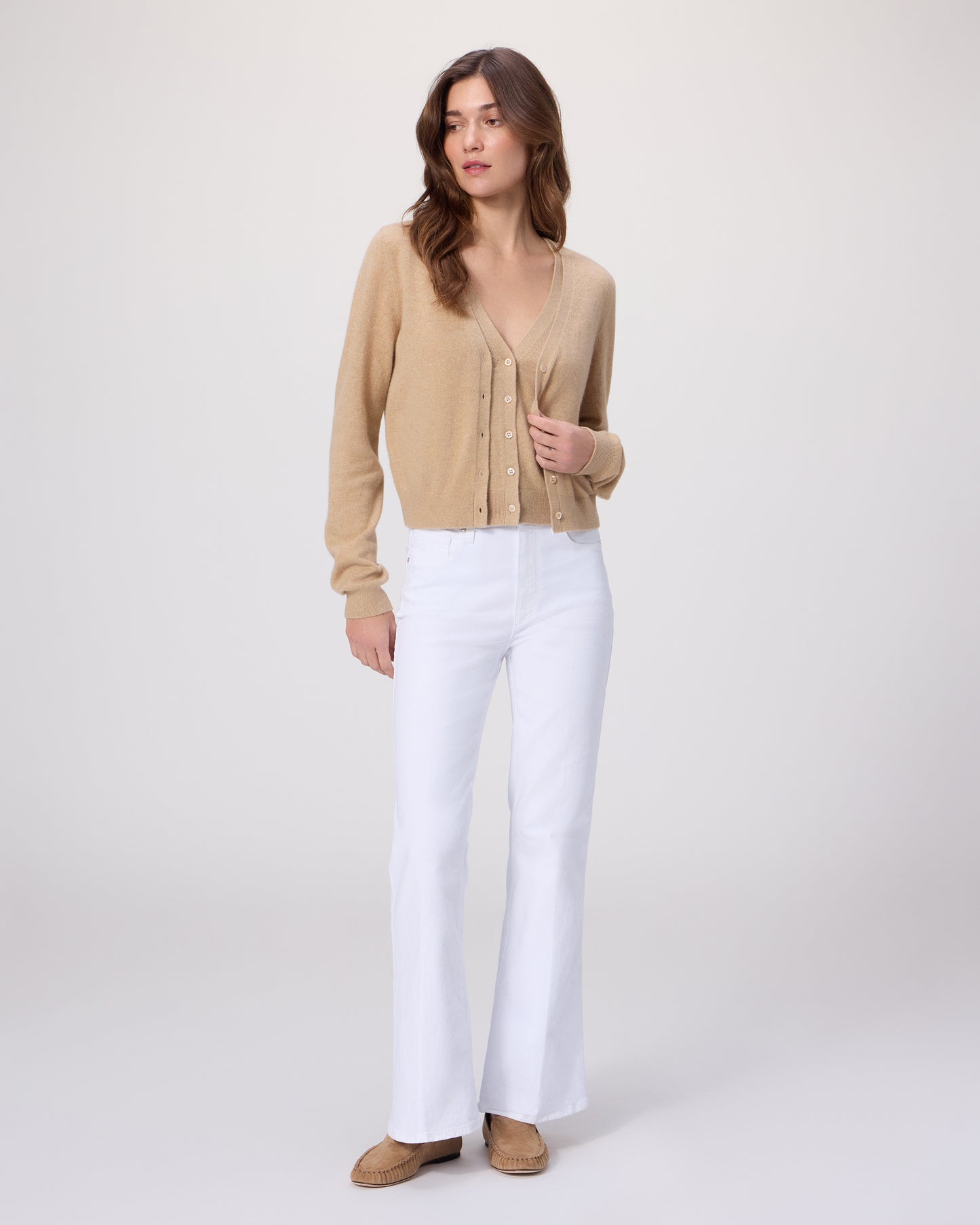 Woman wearing a beige cardigan and white pants on a white background