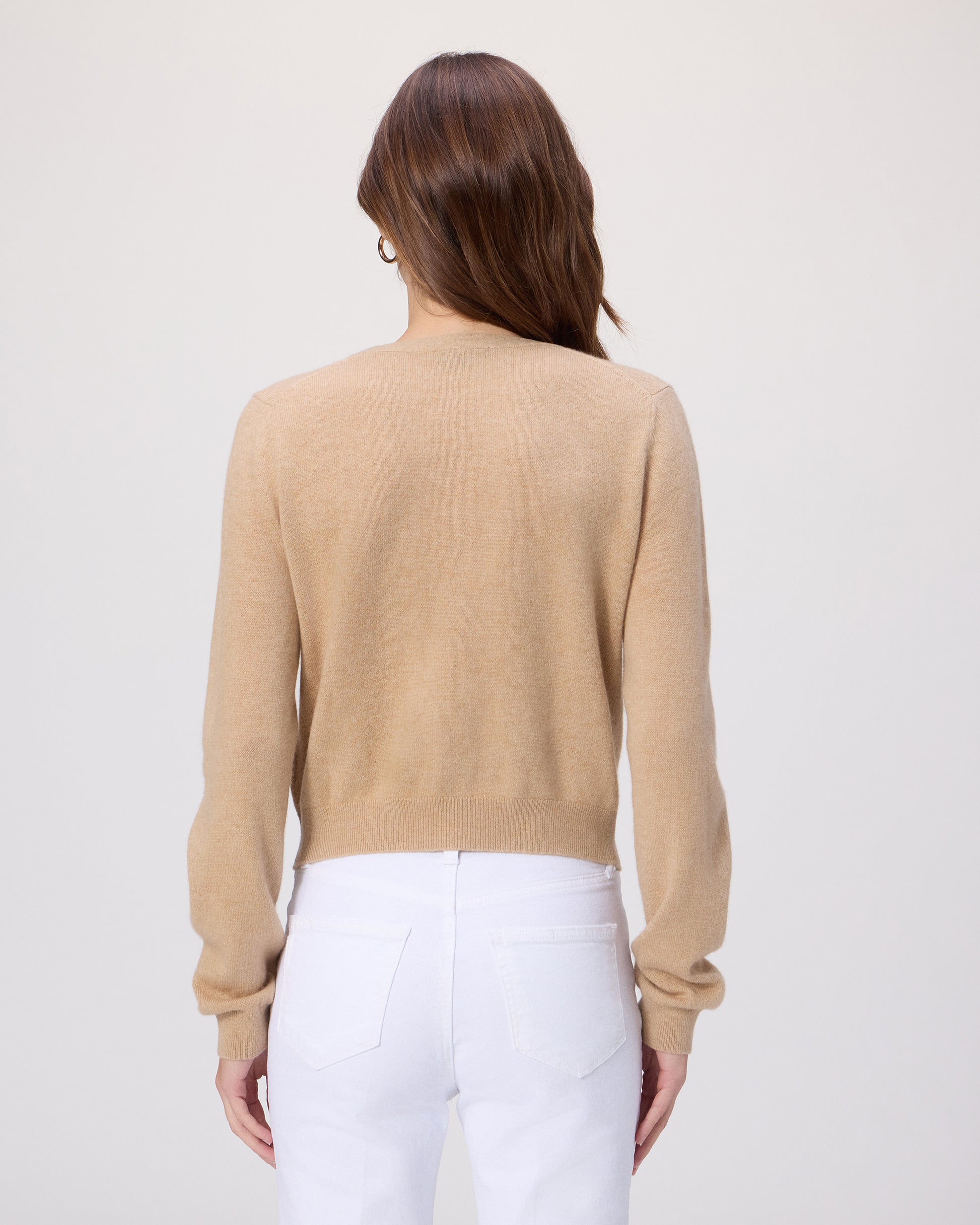 Woman wearing a beige sweater and white pants on a plain background