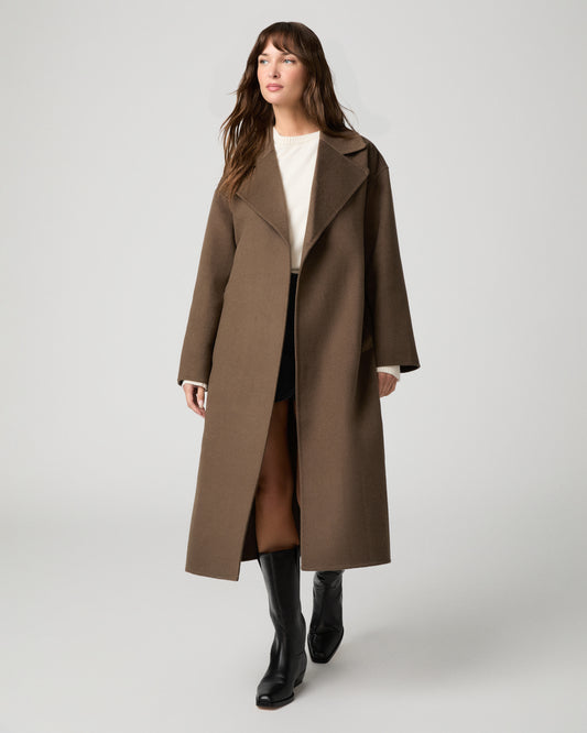 Woman wearing long brown coat and black boots against a white background